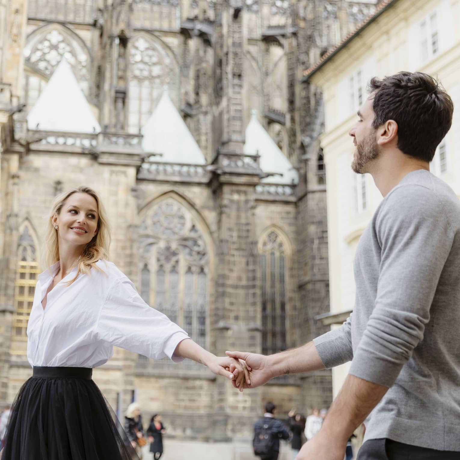 Couple smiling, holding hands with arms stretched as they tour historic city