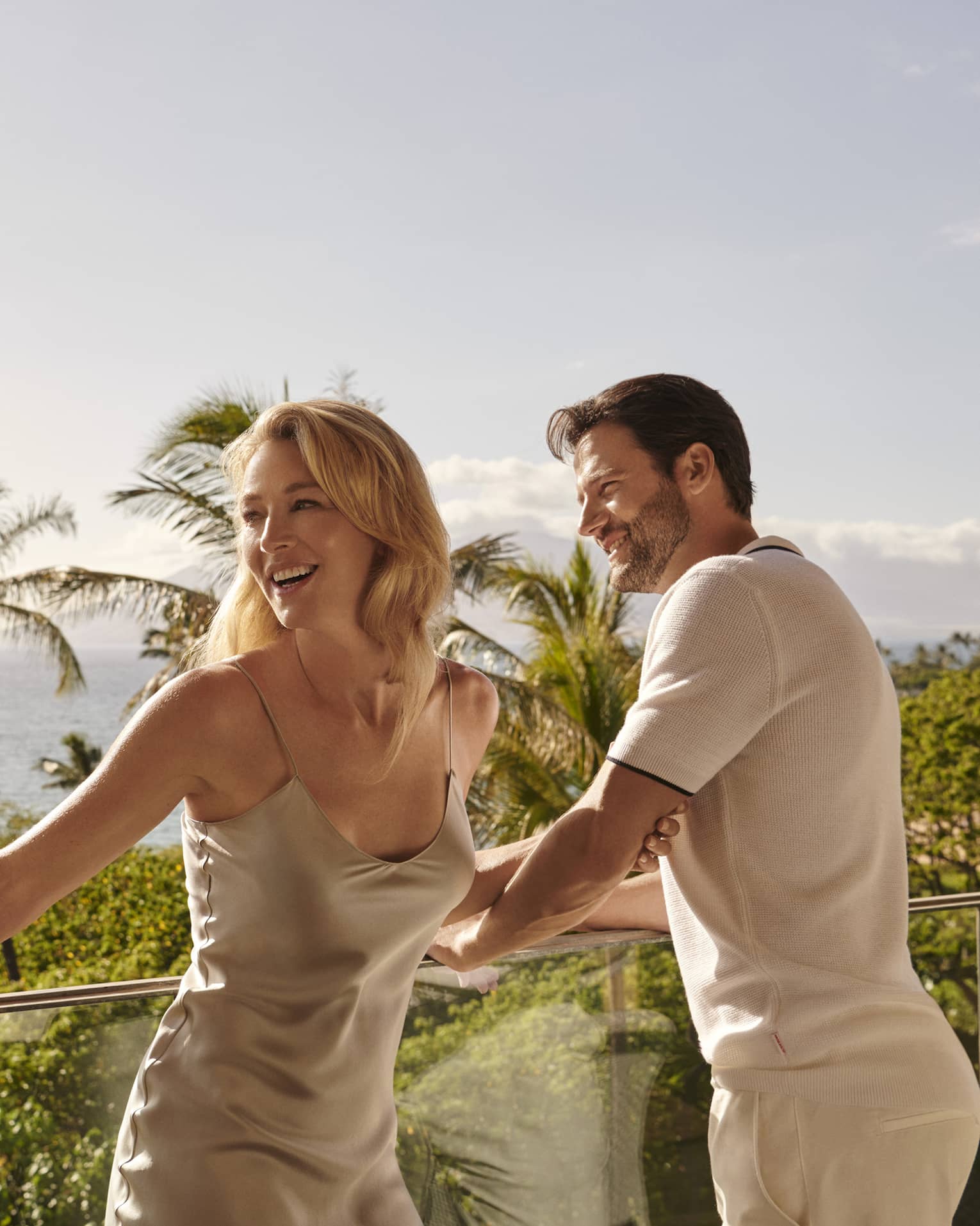 Man and woman enjoy ocean view from balcony with glass railing