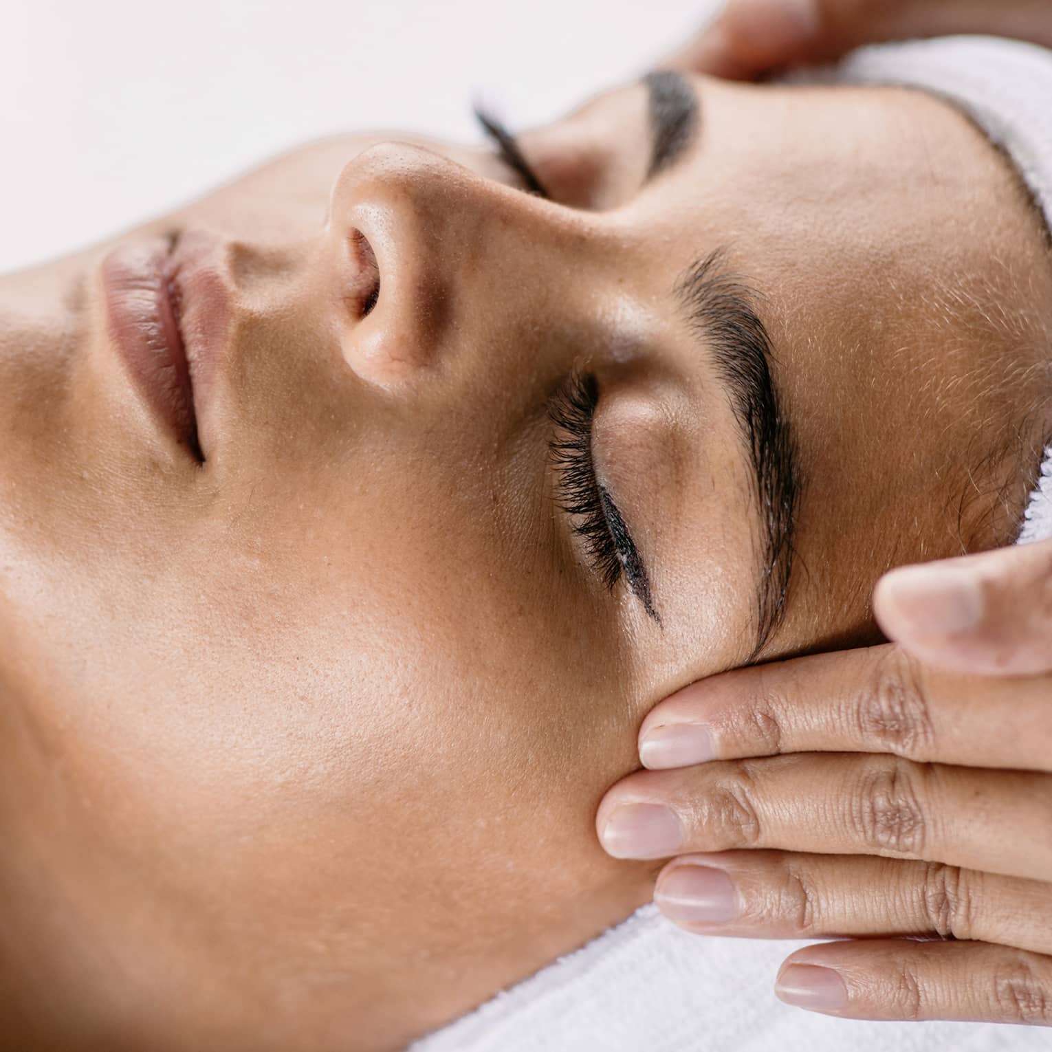 Hands massage woman's temples as she closes her eyes, spa towel around hair