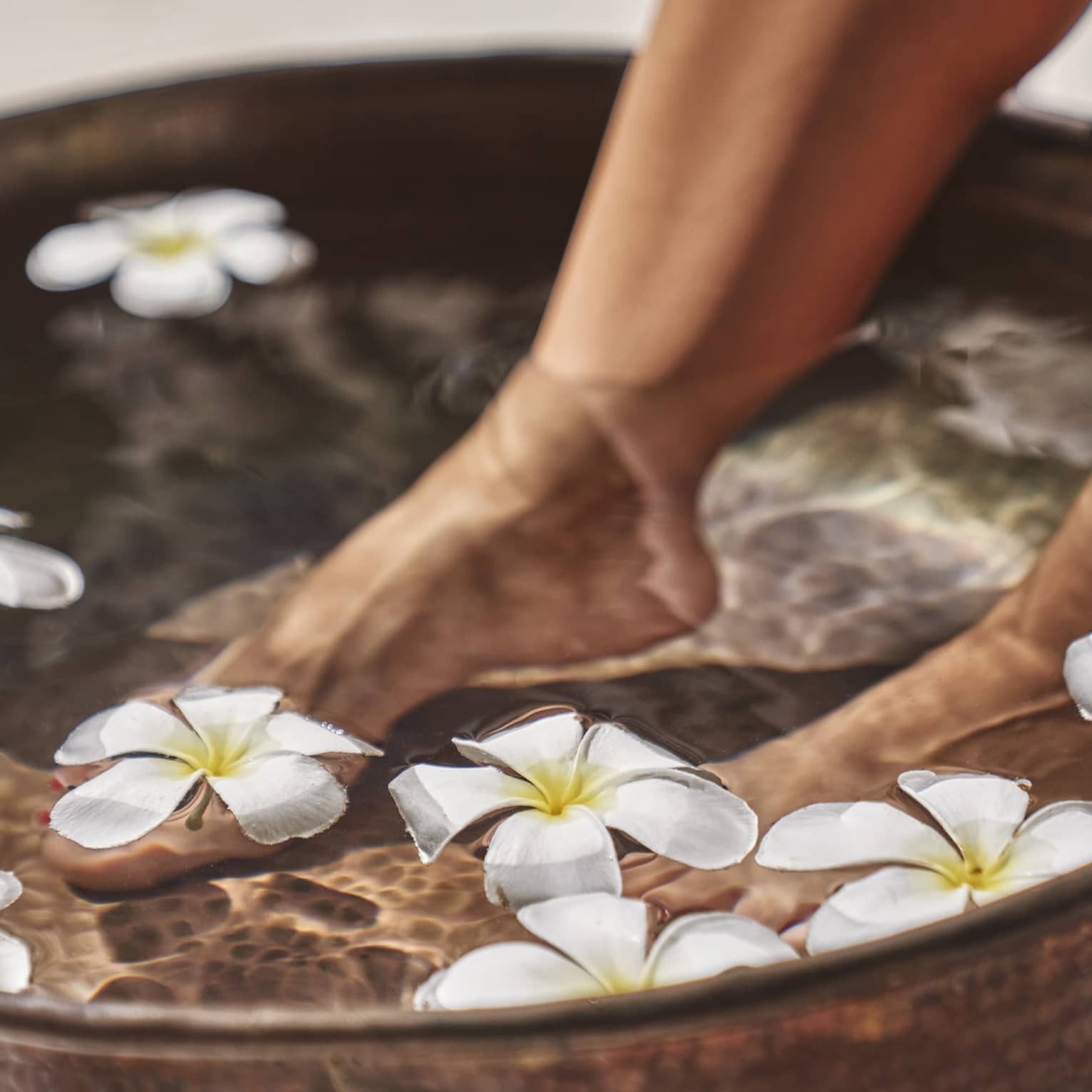 A woman's feet in a bowl of water and flowers.