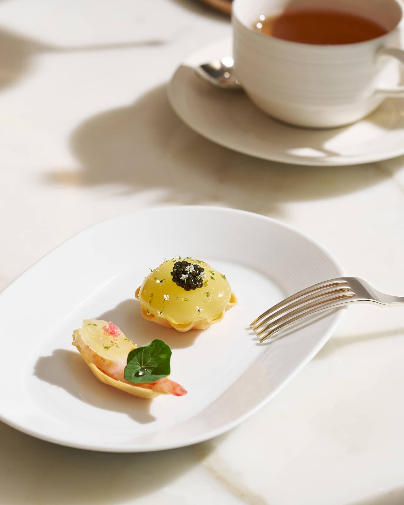 Two colourful pastries on a white plate, with a cup of hot tea in the background