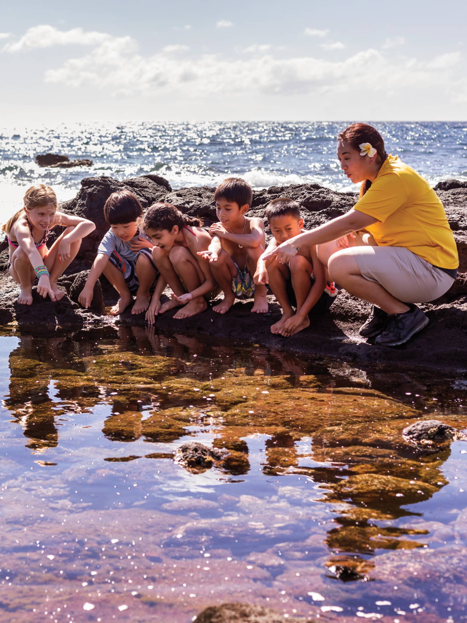 Children perched on rocks as hotel staff points to pool of water in lagoon