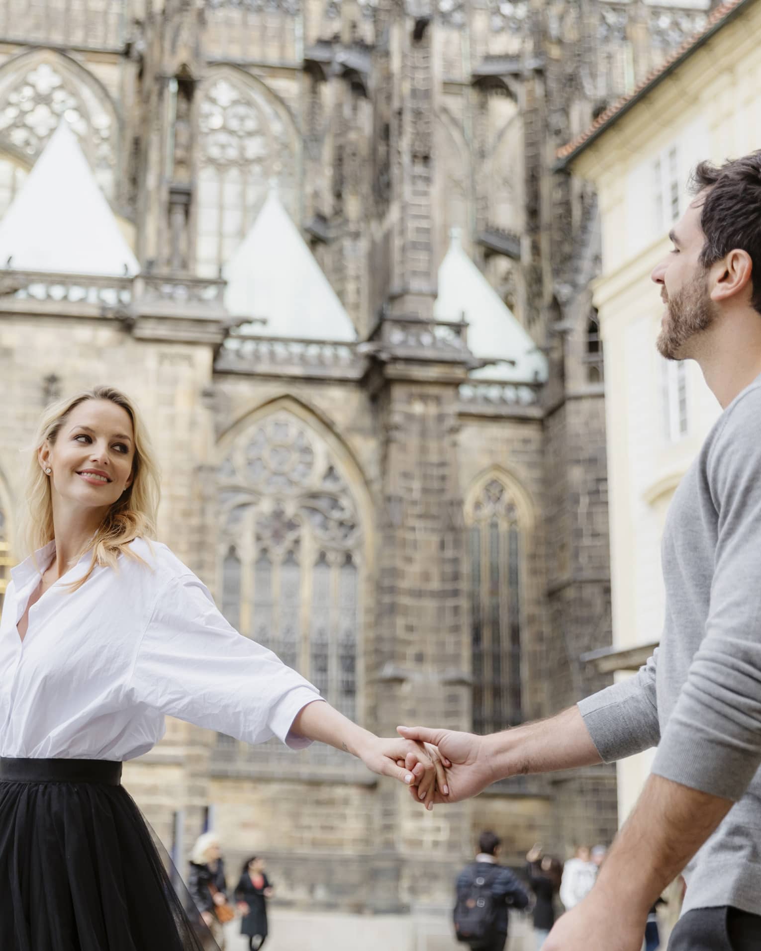 Couple smiling, holding hands with arms stretched as they tour historic city