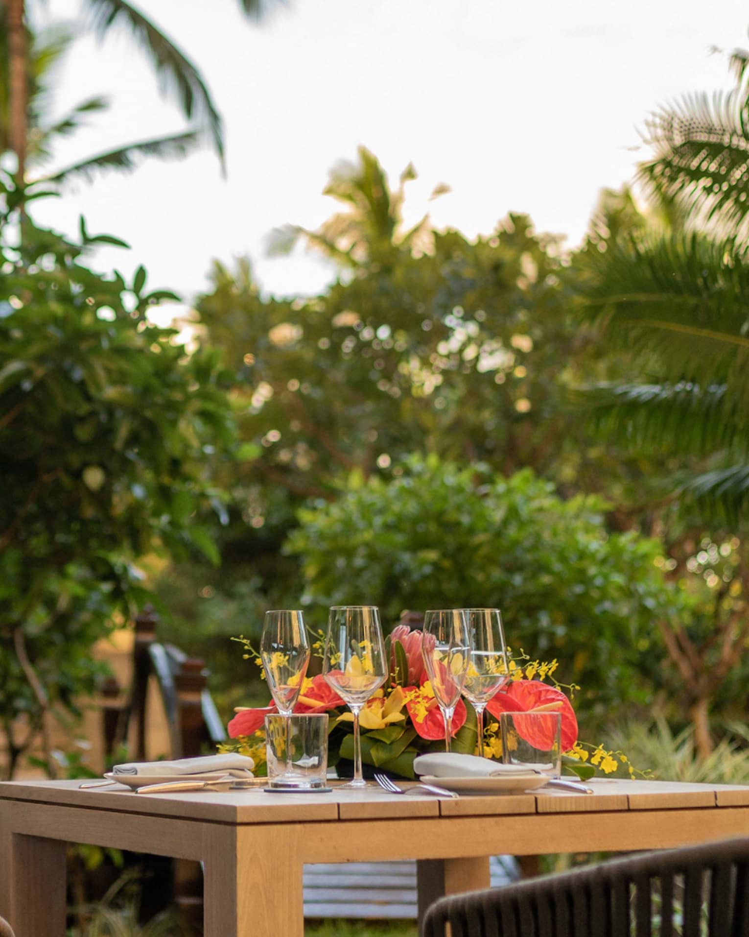 Wooden table set for a two-person dinner in private, tropical garden setting