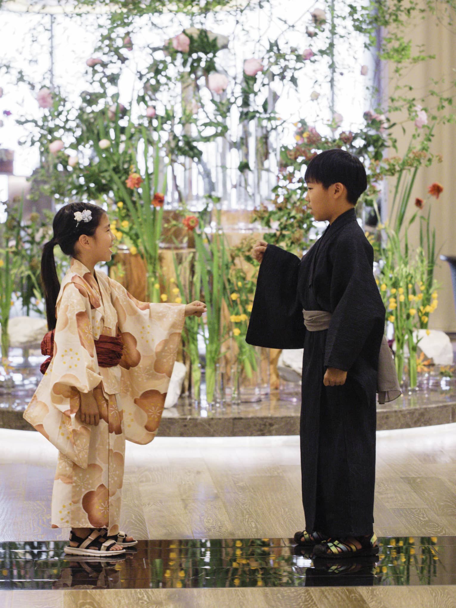 Two children dressed in yukatas stand in hotel lobby in front of elaborate floral floor display