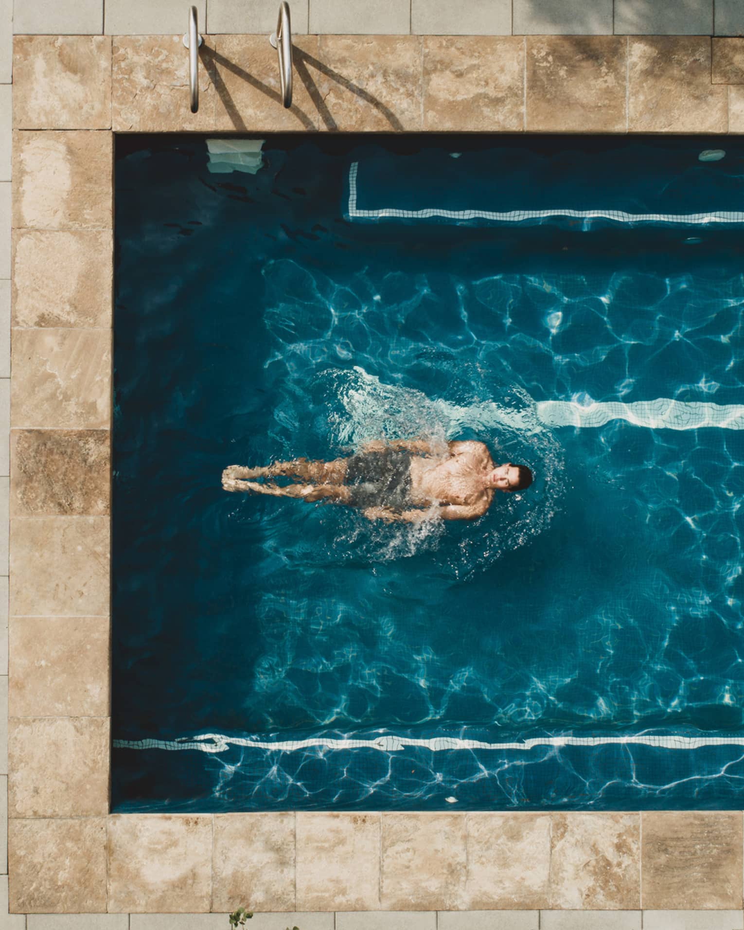 Woman laying in pool chair while man swims in pool.