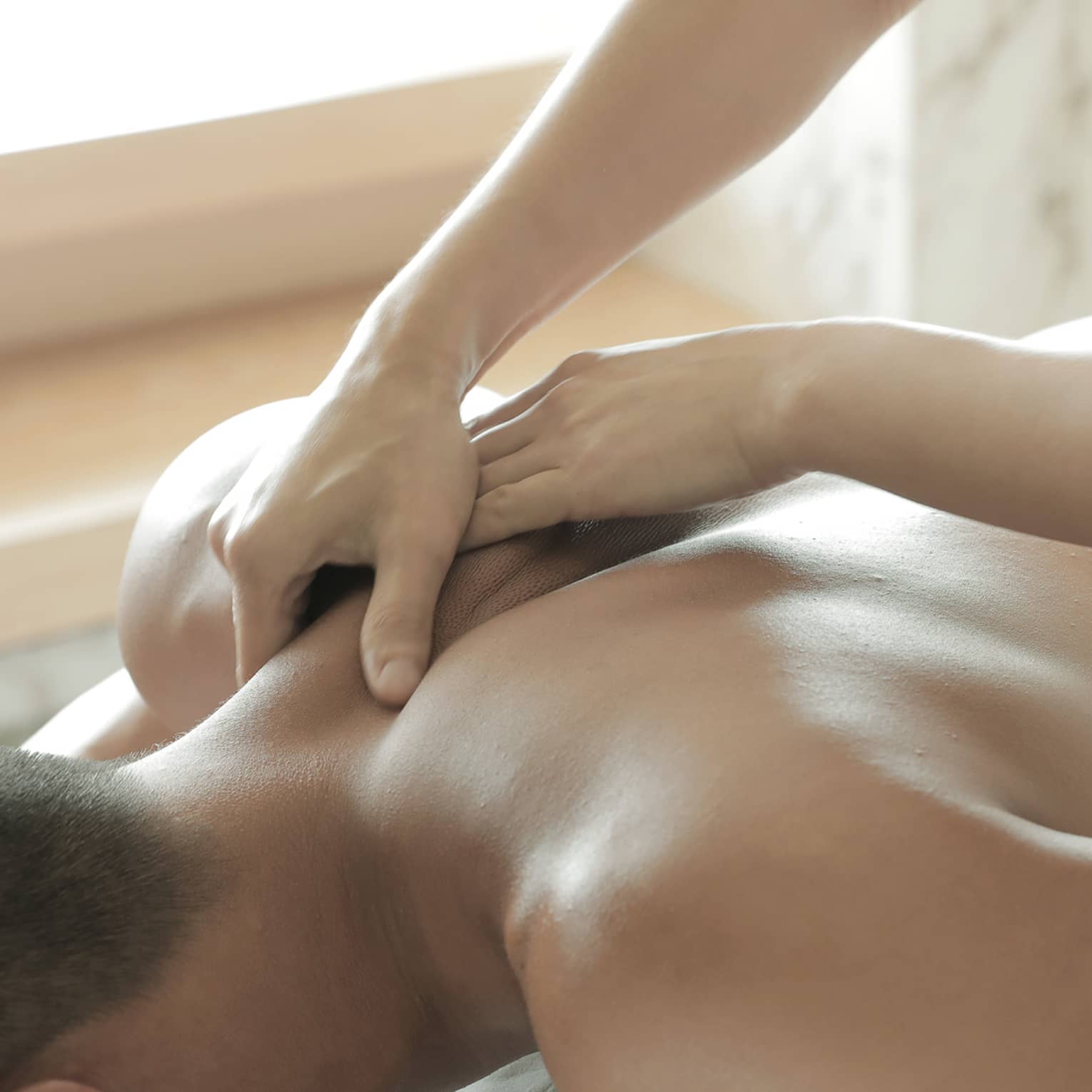 Spa masseuse massages man's bare back, shoulders
