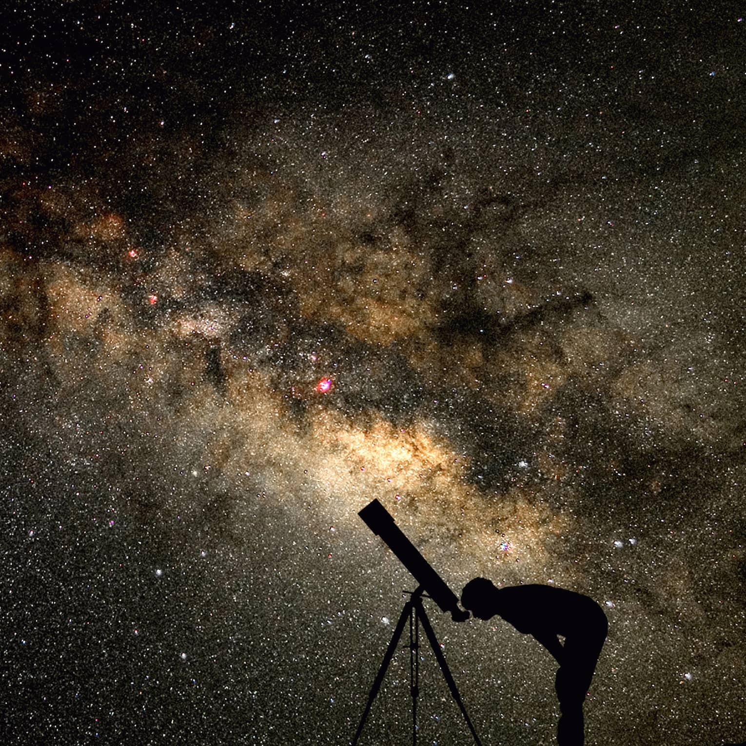 Silhouette of stargazer leaning into telescope against a starry sky, milky way