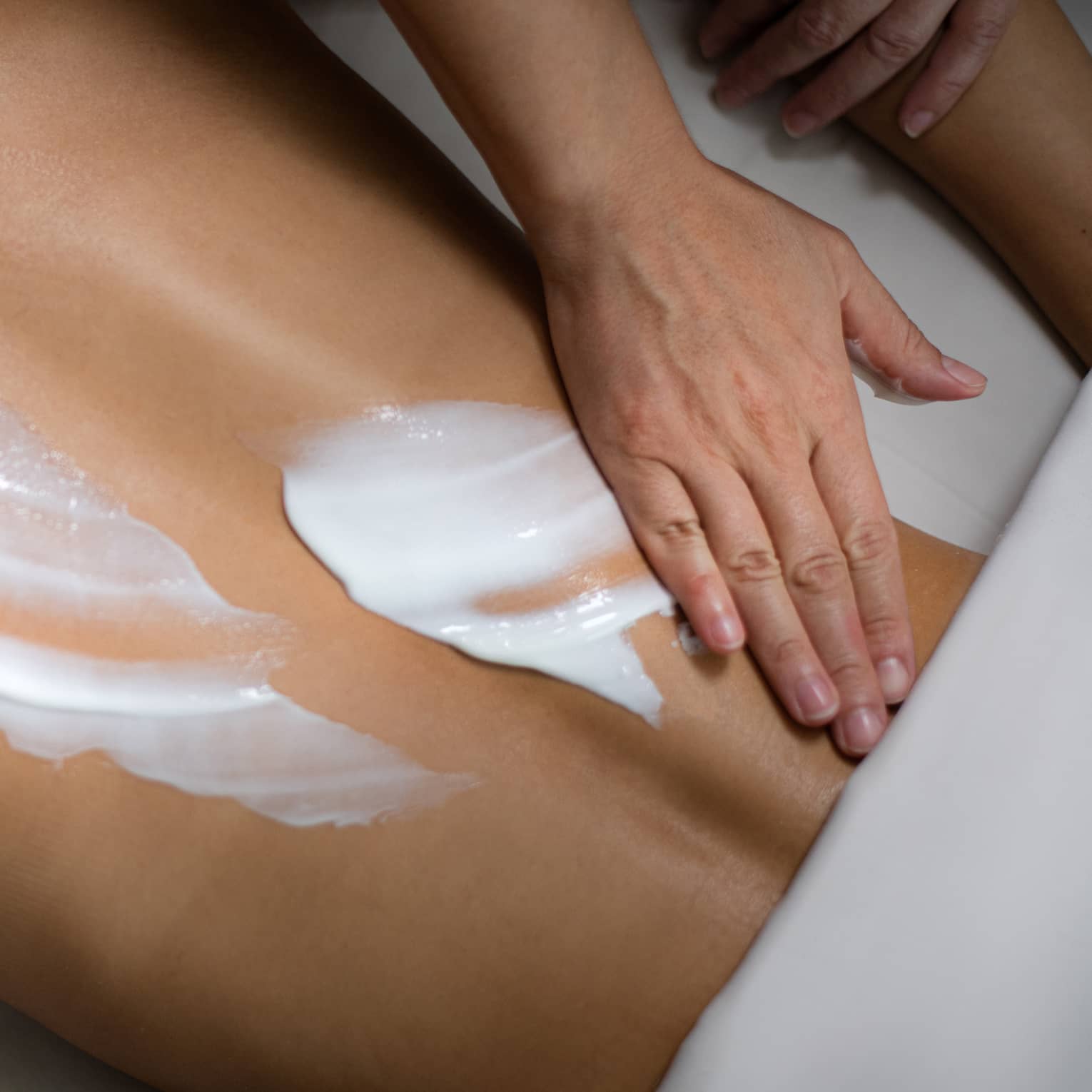 A person rubbing white lotion onto a woman's back.