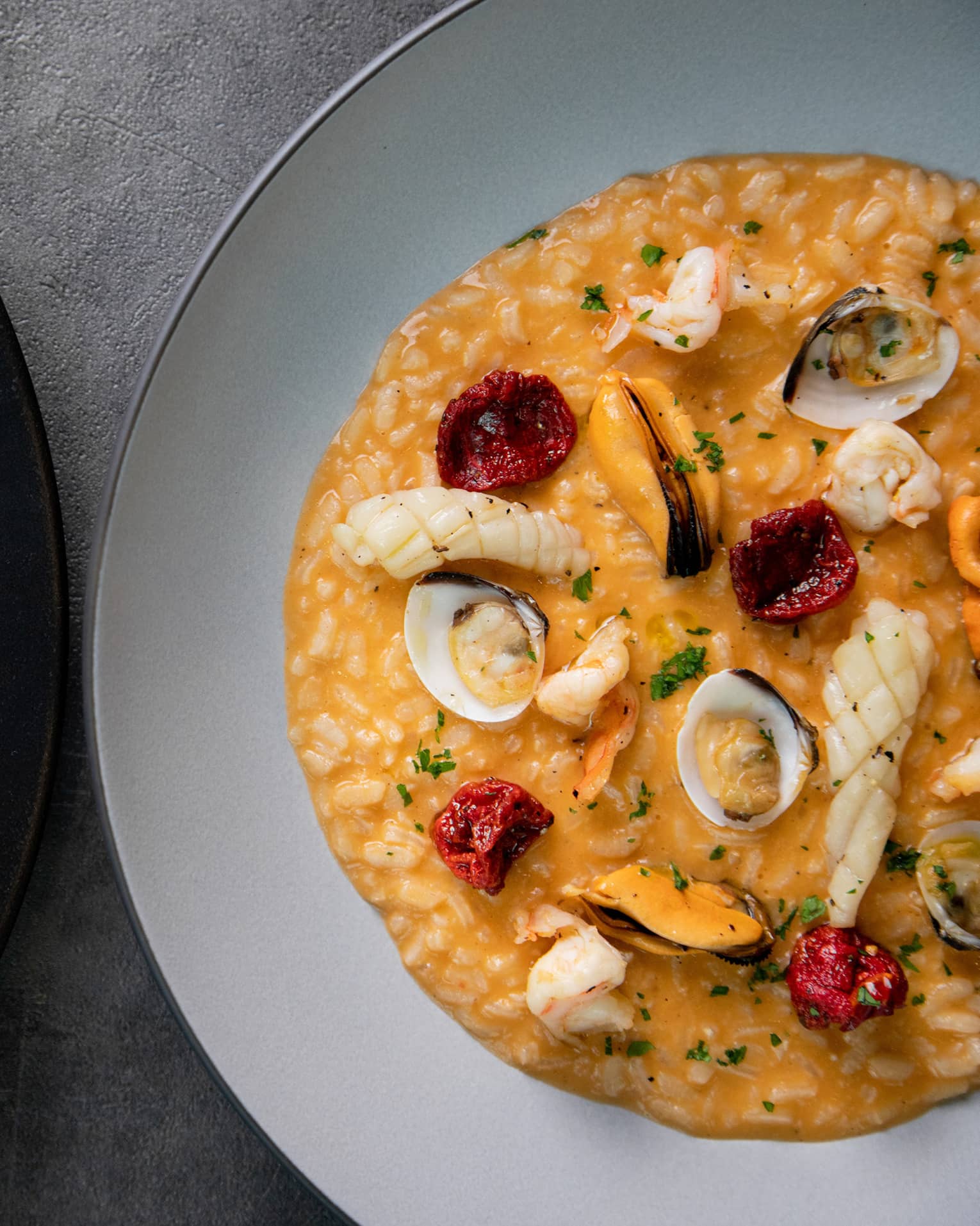 Two risotto dishes, one seafood on white plate and one Italian on black plate