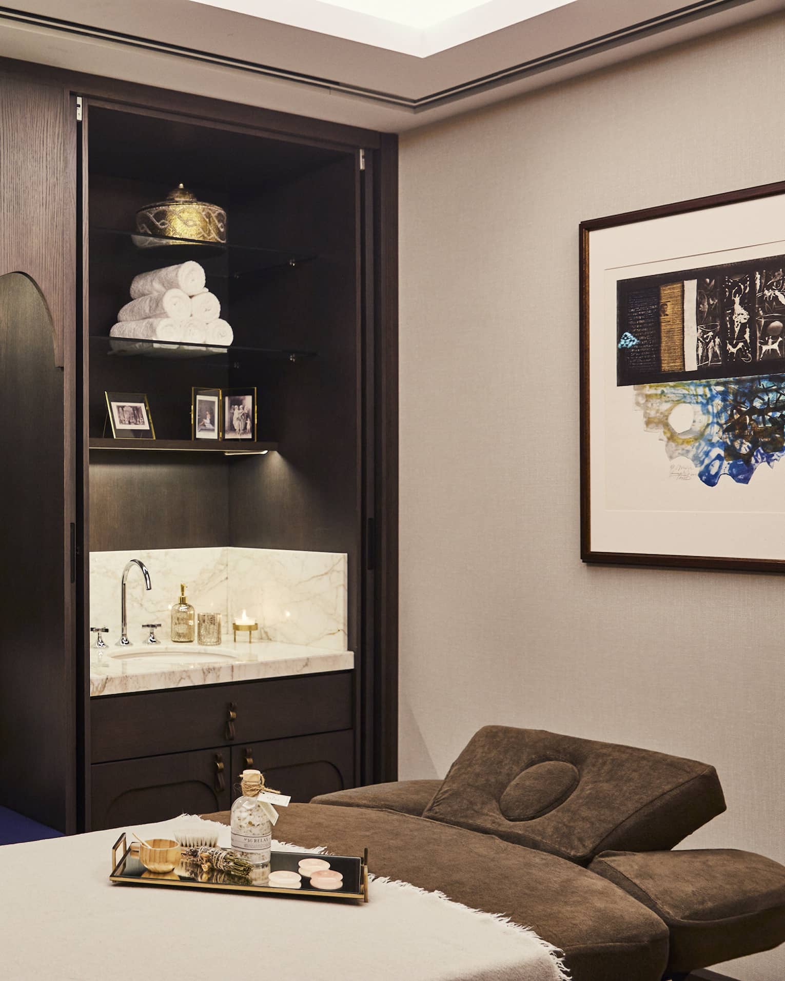 Kuma Spa treatment bed with tray with oils next to large wood cabinet with pillows and sink