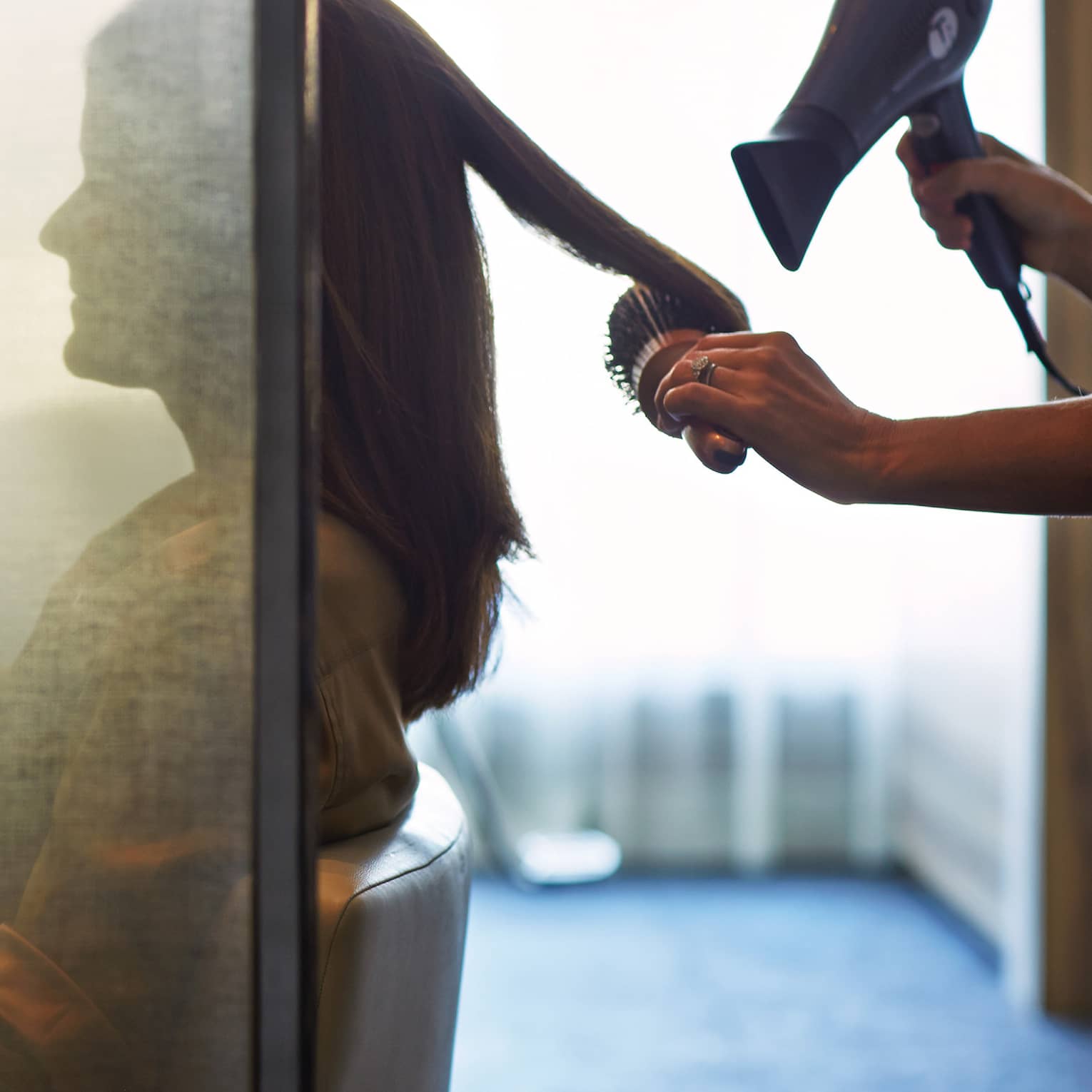 Silhouette of woman behind salon screen as hairdressers brushes, blow dries hair