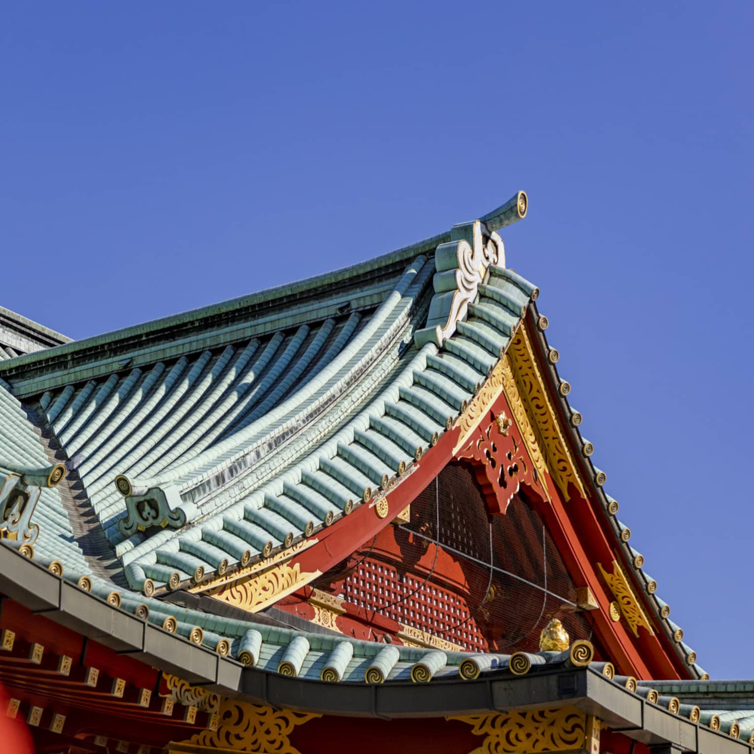 Concave tented gable rooftops of Shinto temples with ornate red and gold facades and grooved piping on the roofs.