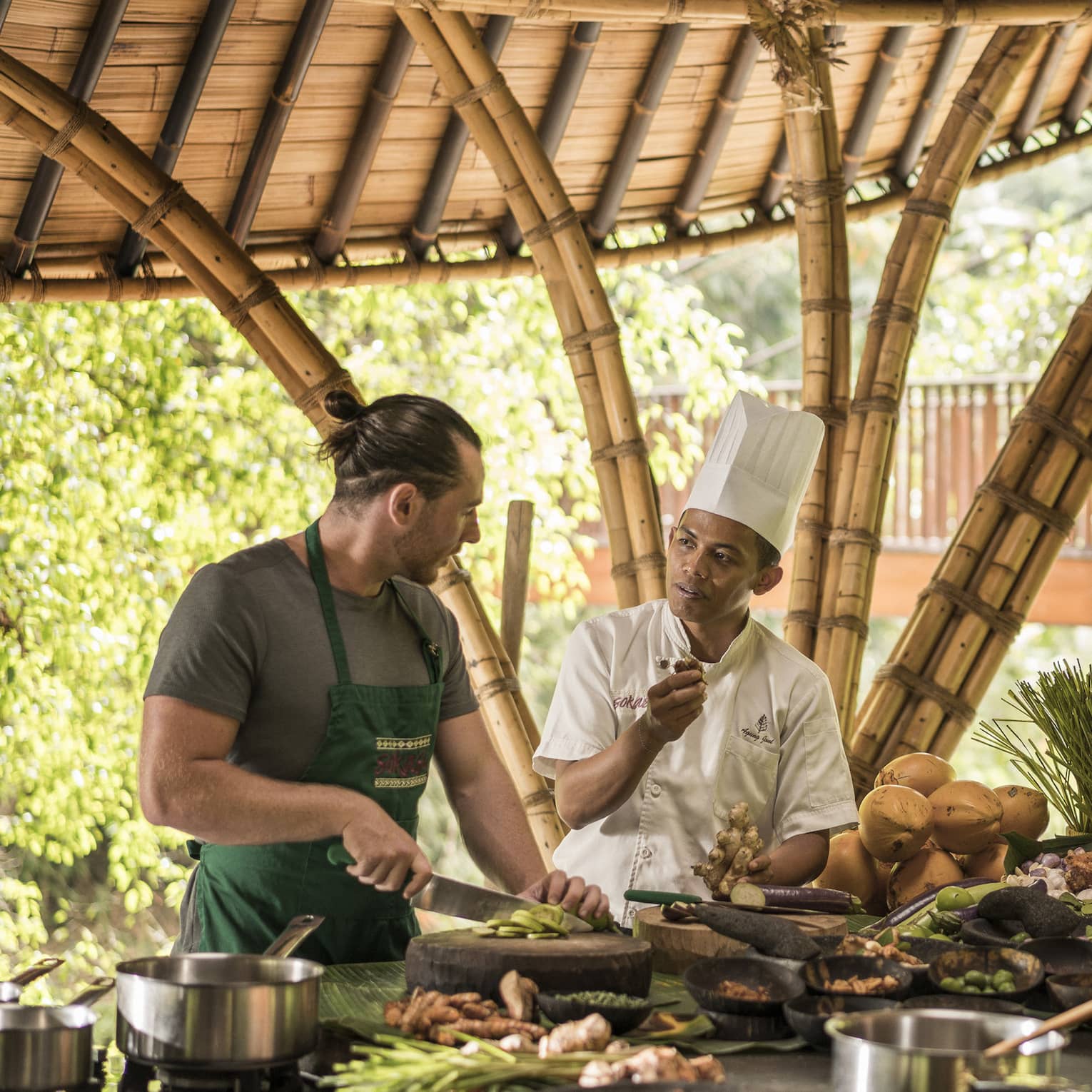 A four season chef instruction a man and woman how to cook in an outdoor kitchen