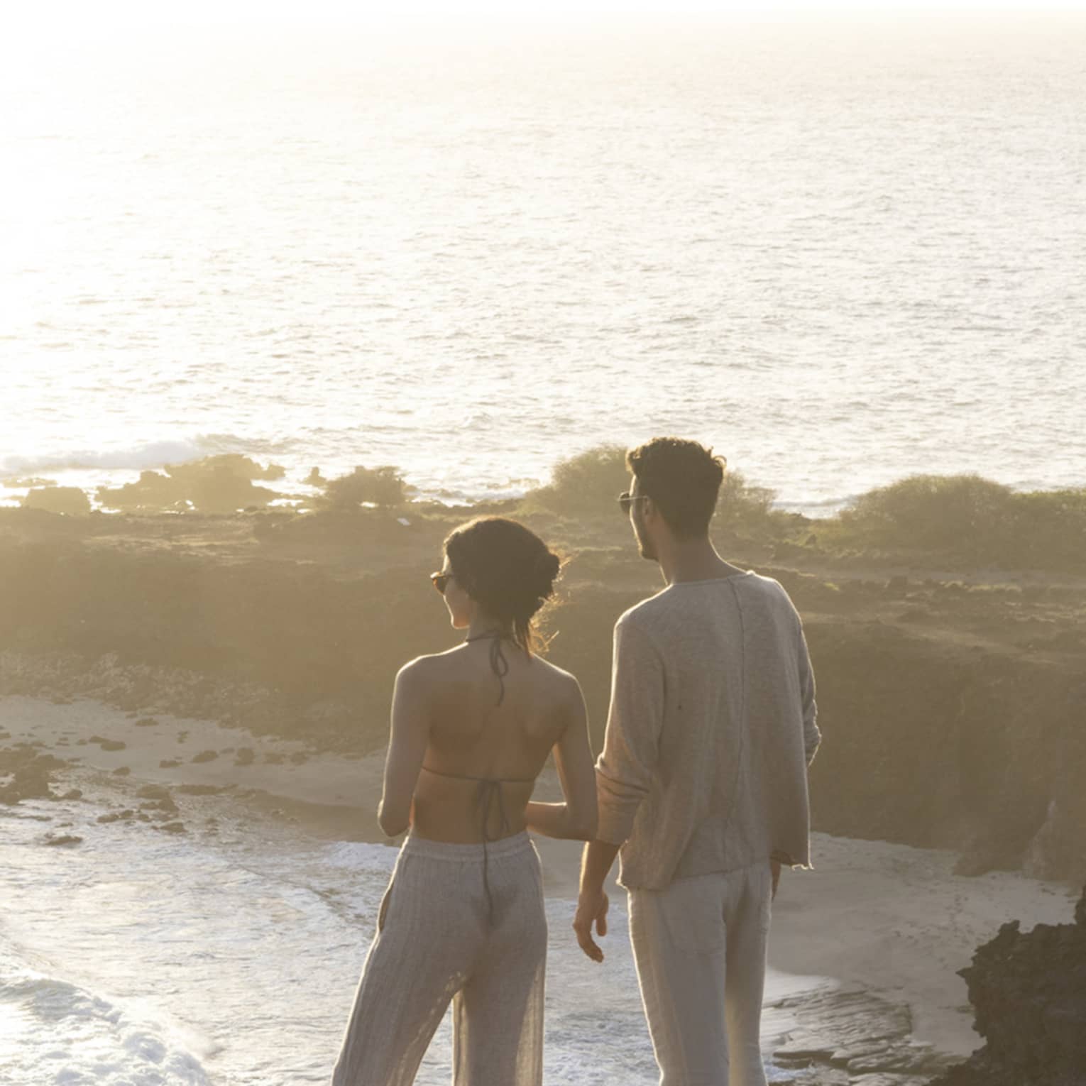 A man and woman stand on top of a cliff overlooking bay in Hawaii