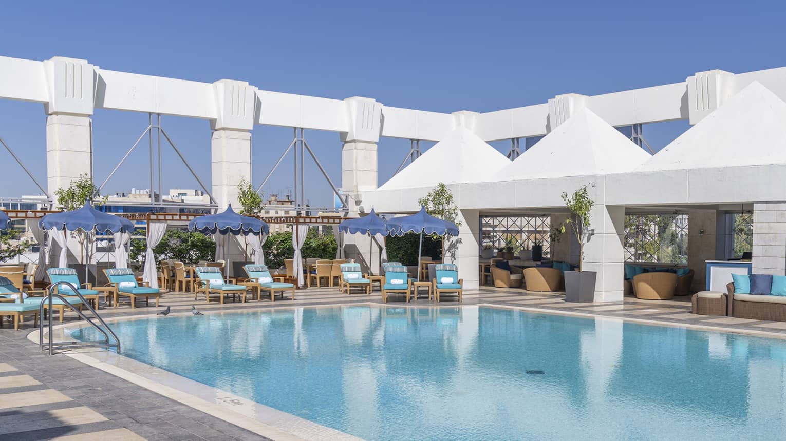 Outdoor pool surrounded by blue lounge chairs and four white tents