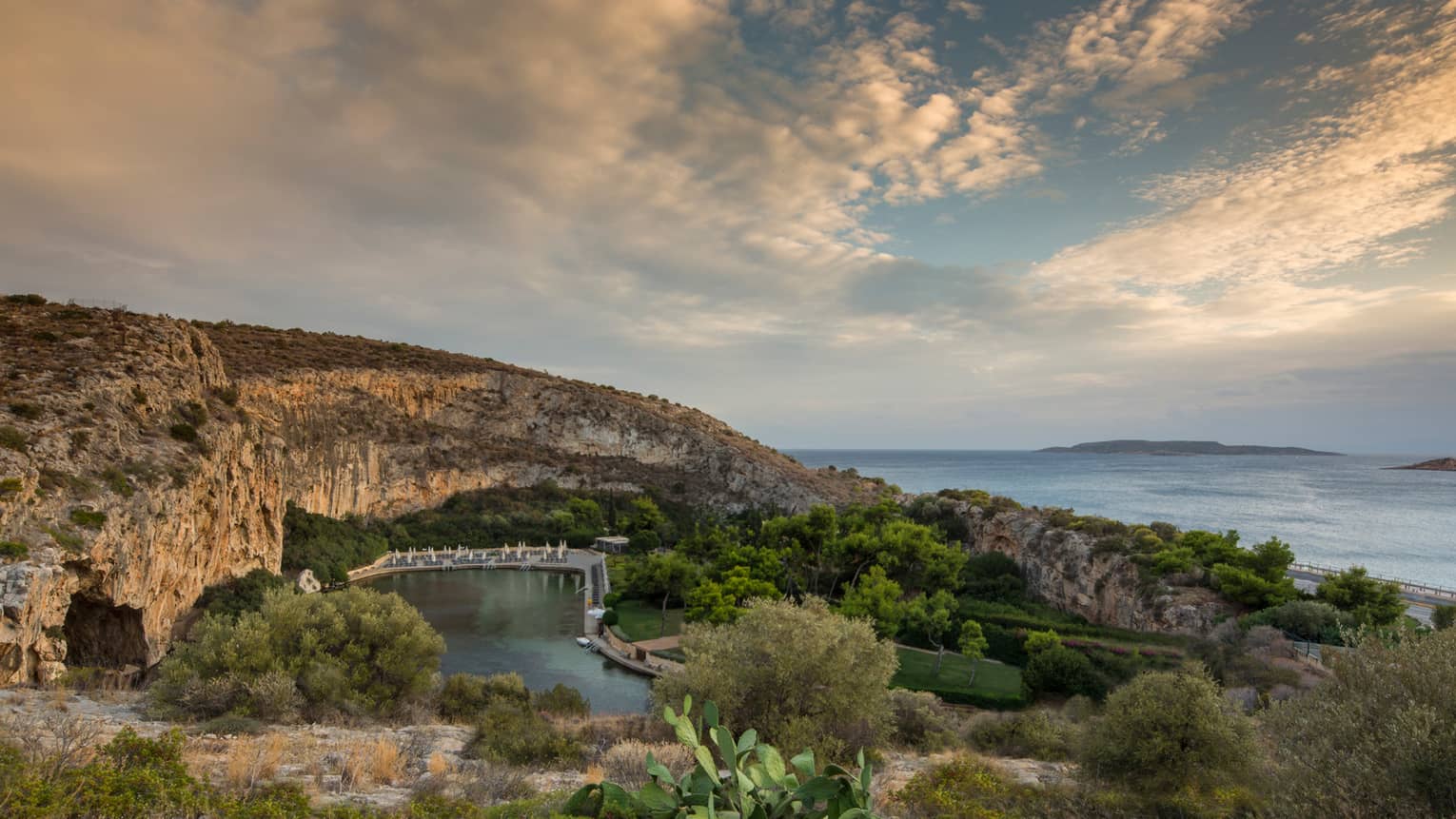 View of Vouliagmeni with rocky hill, green trees and shrubs overlooking ocean