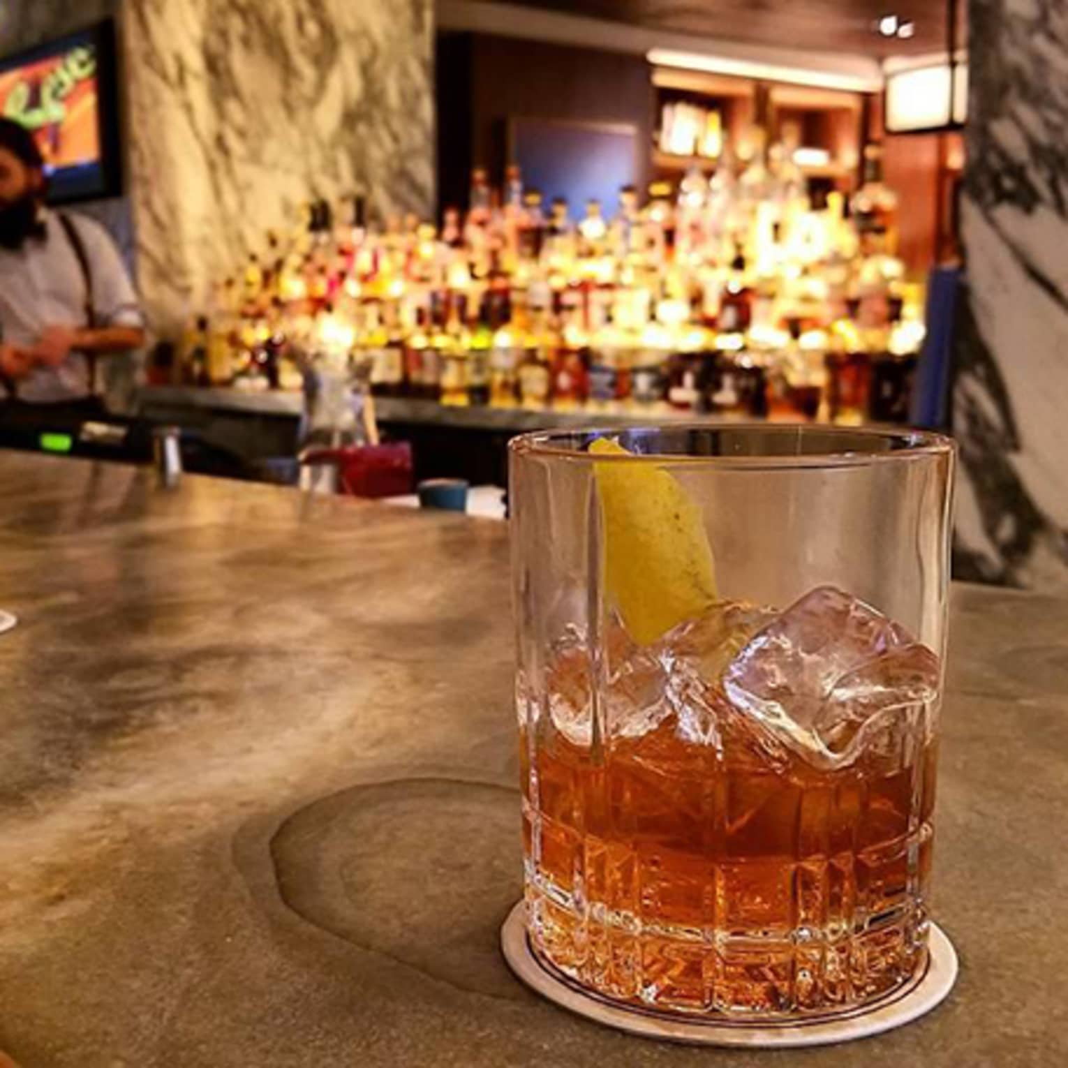 Cocktail with ice in rock glass on bar, two mixologists in background