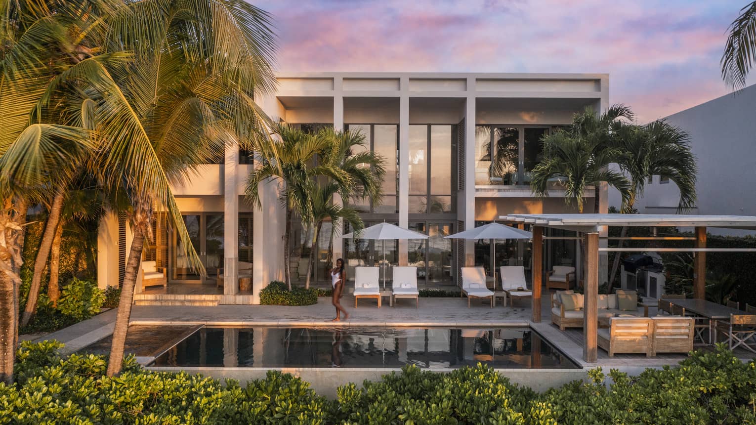 Luxury beachfront villa with pool, palm trees, sun loungers and a person walking at sunset