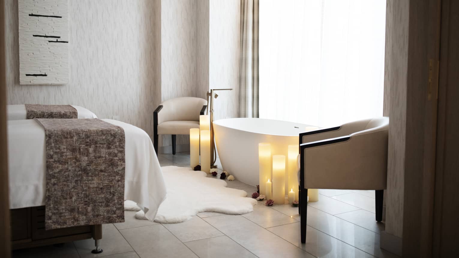 A spa room with two massage beds, a bath rub and two chairs.