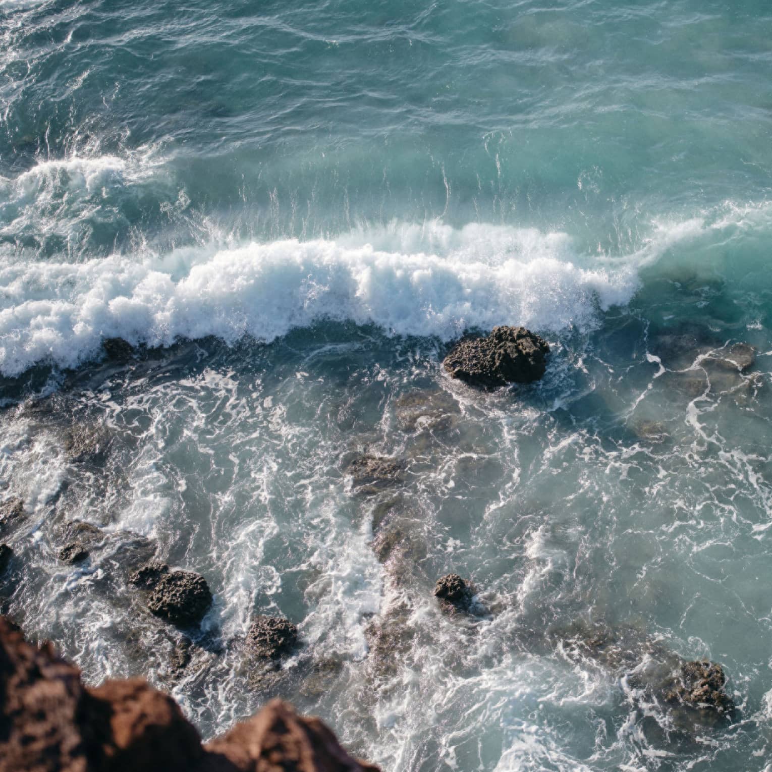 Aerial view of an ocean wave breaking over a rock formation