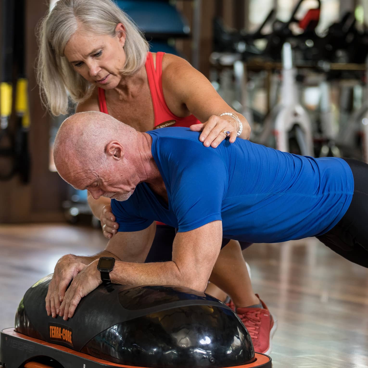 Fitness trainer helps man balance on pilates board in exercise studio