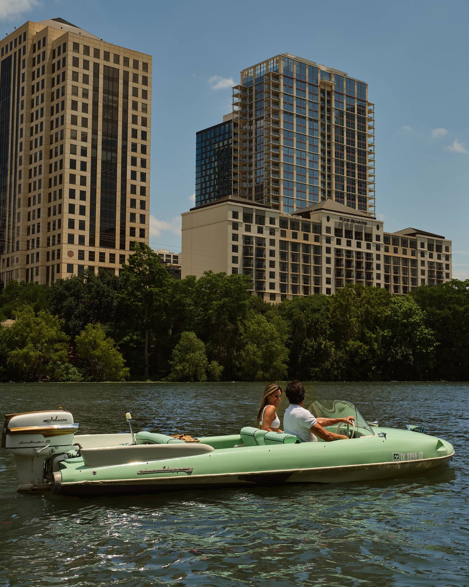 Two guests on a boat in the water with city buildings in the background