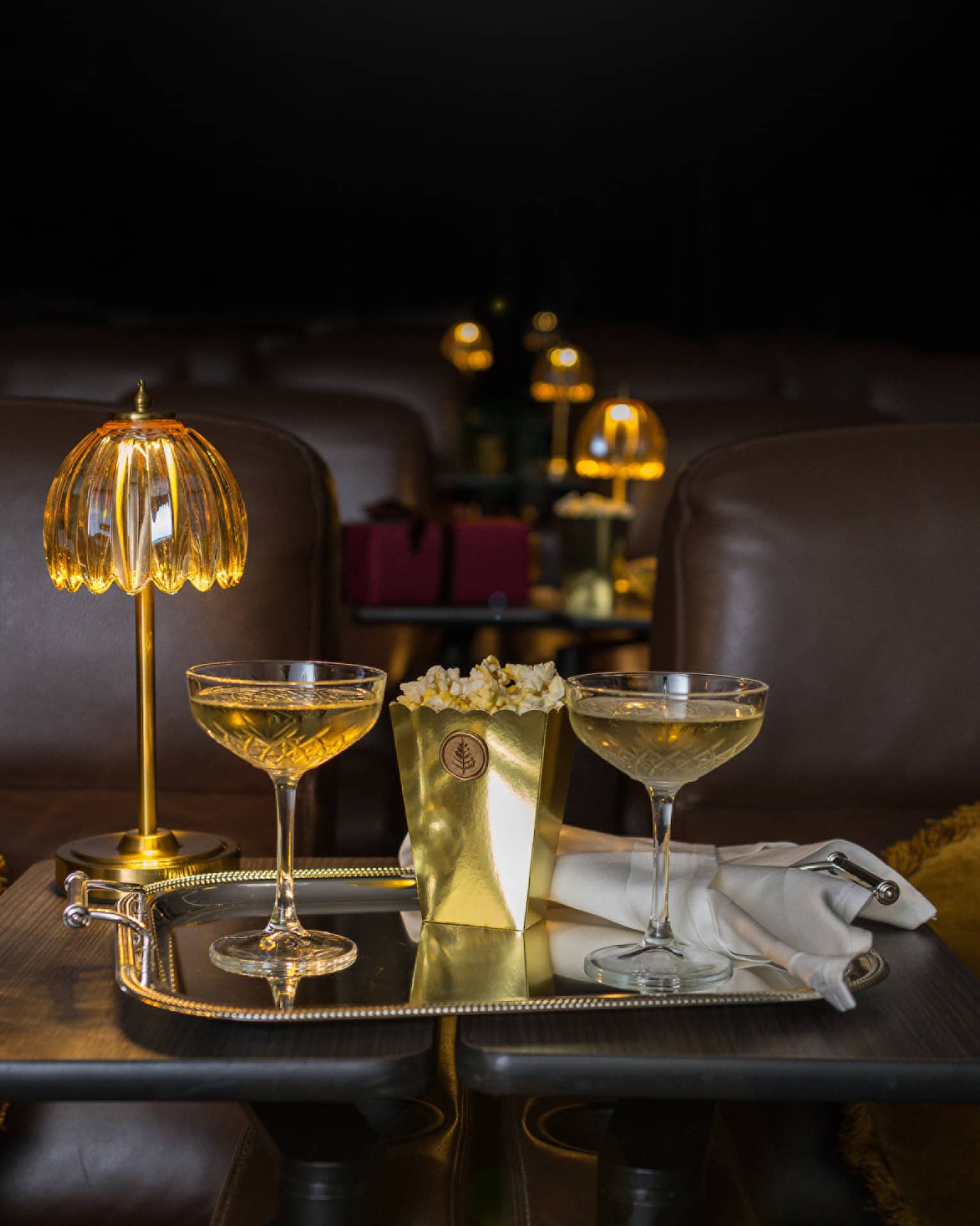 Two filled coupe glasses on a silver serving tray with popcorn in front of a golden dome light.