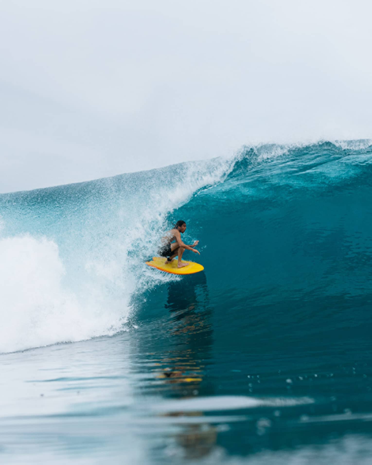 Person on yellow surfboard ducks underneath wave in the middle of the ocean
