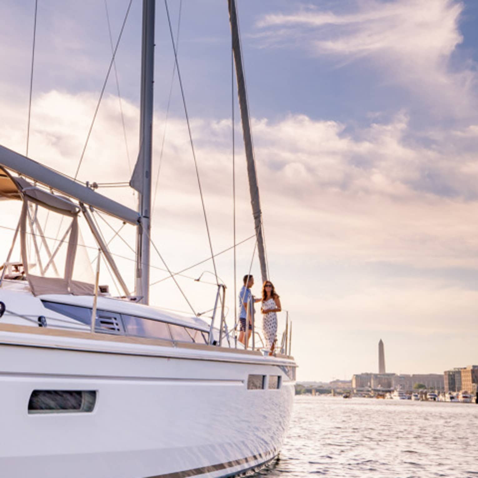 Two guests standing on a boat in the water with a view of the city in the background.