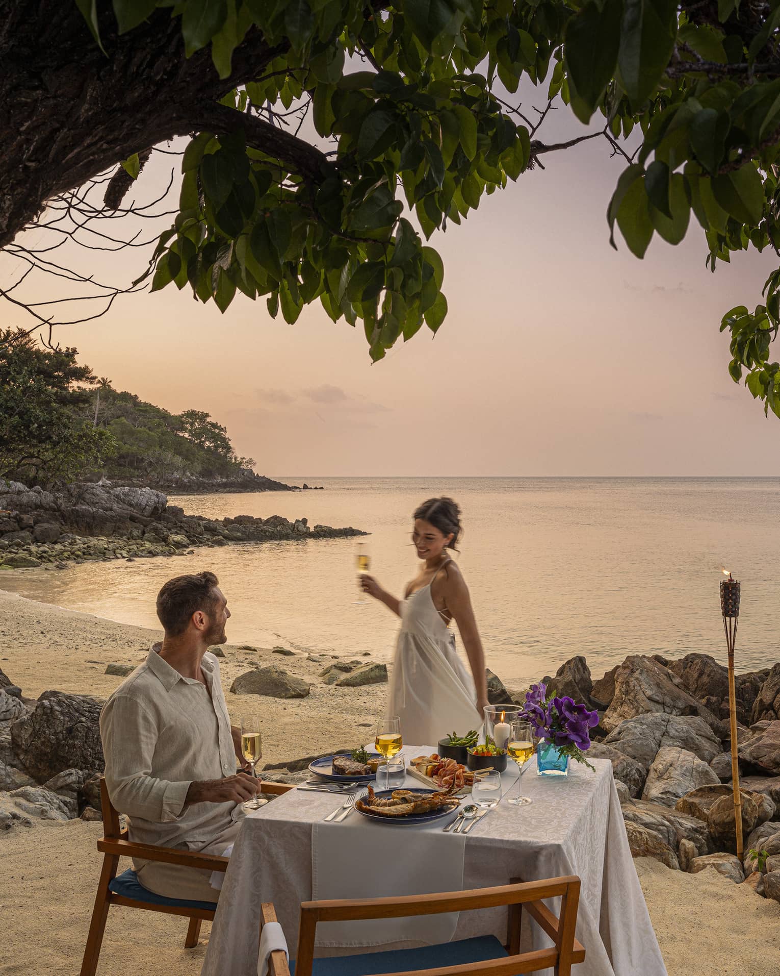 A beach dinner date at dusk, with a couple enjoying a serene seaside view.