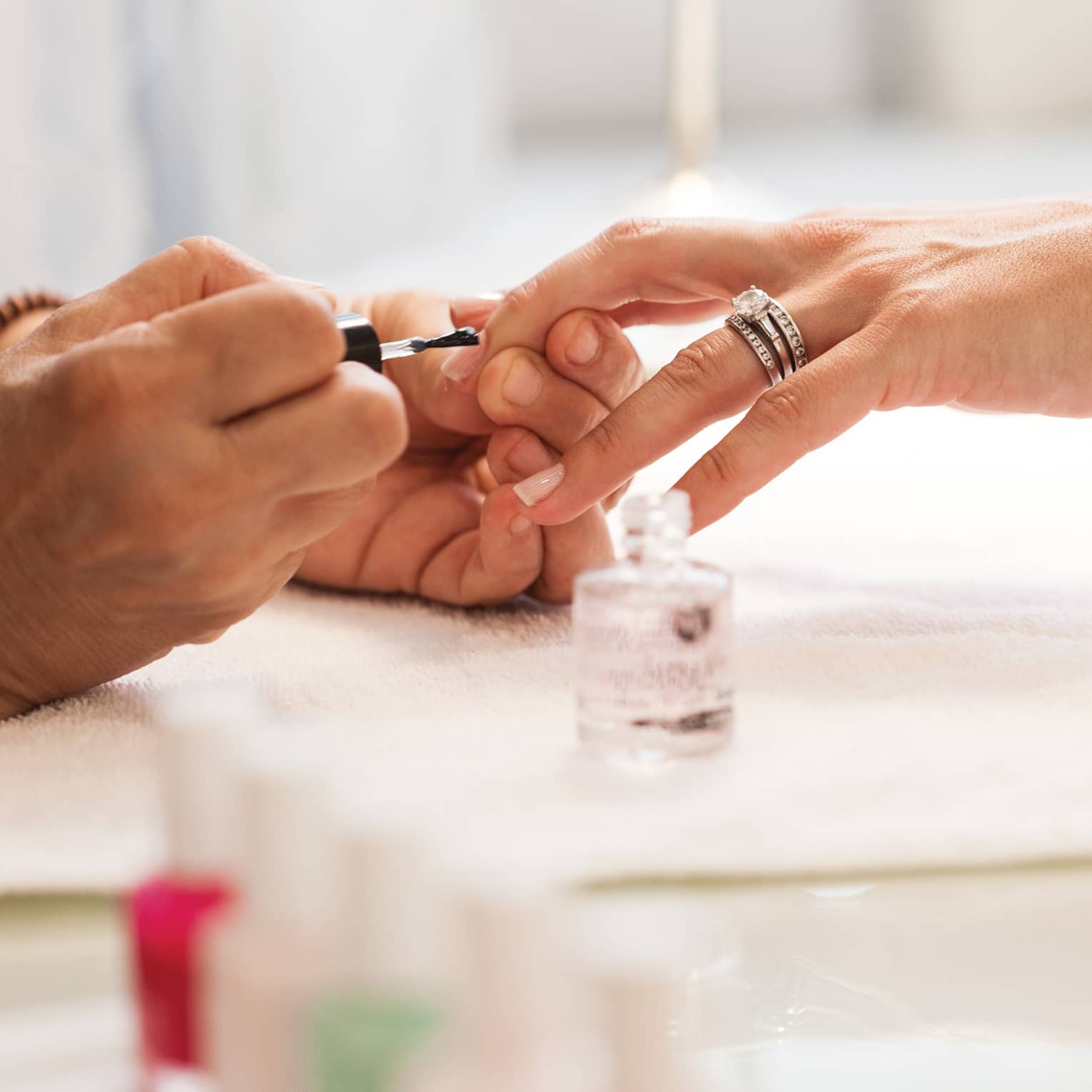 Close-up of woman in white robe getting clear polish manicure at spa table