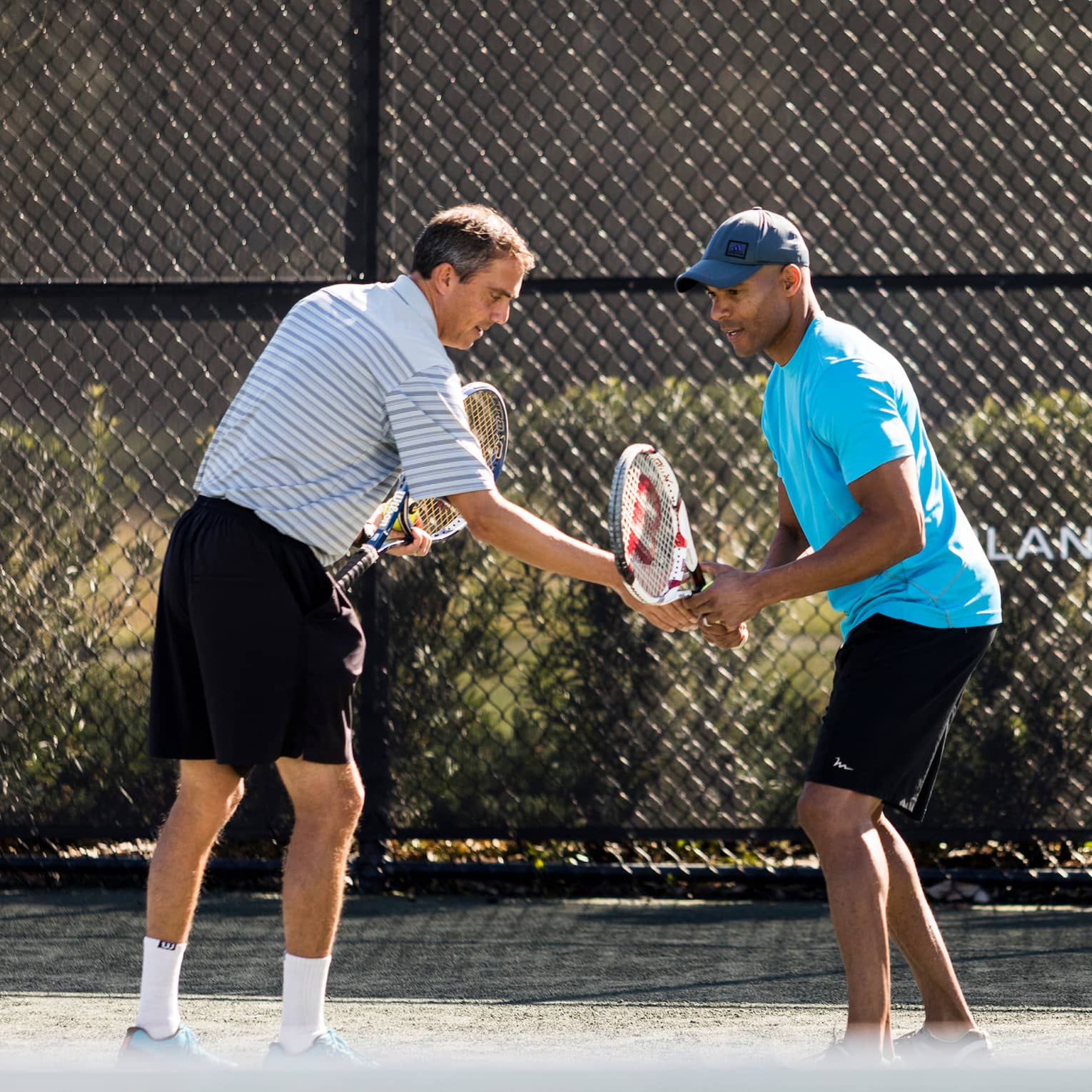 Tennis pro helps man adjust his racket on tennis court by Four Seasons Resort logo on fence