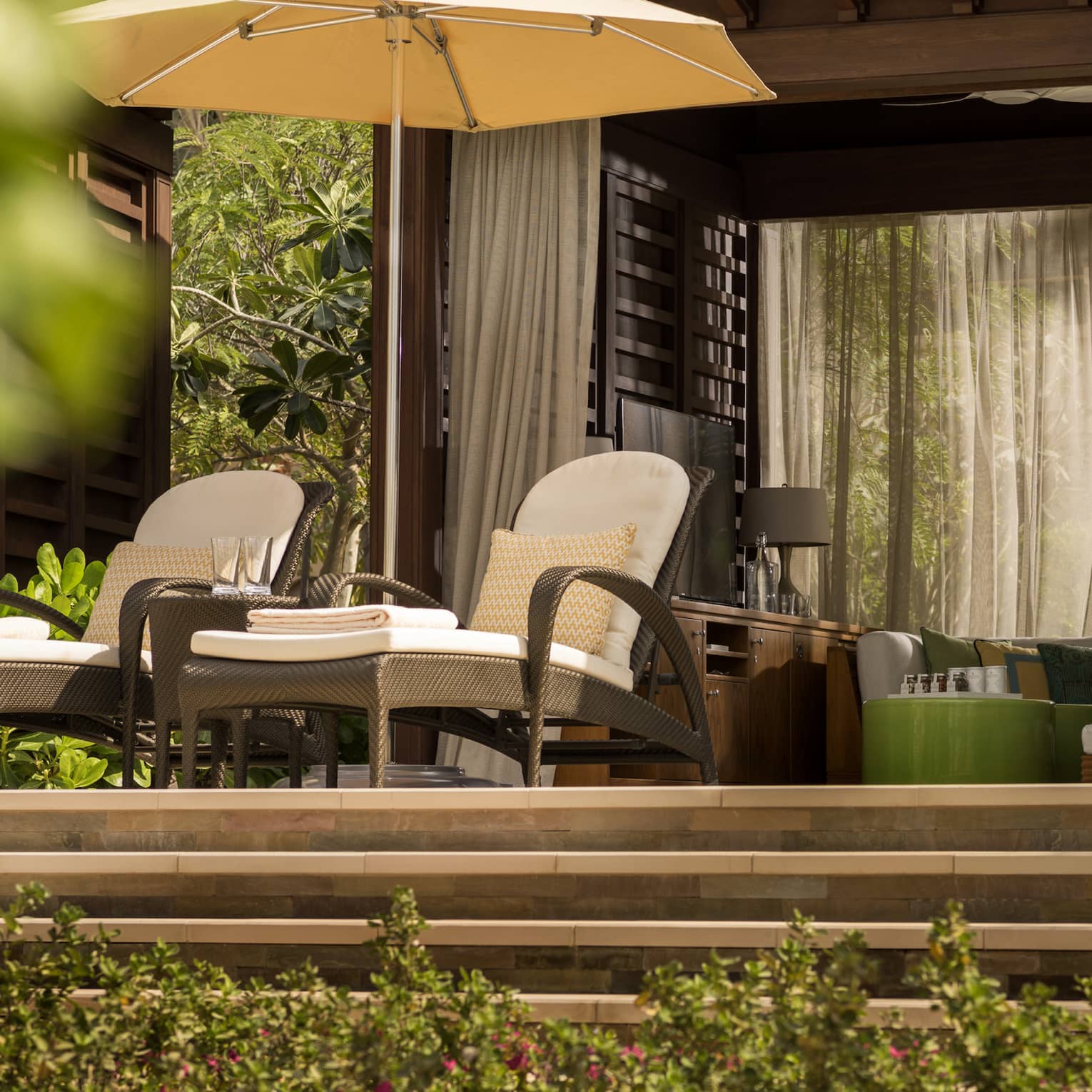 Two wicker chairs on a patio above several flowery bushes.