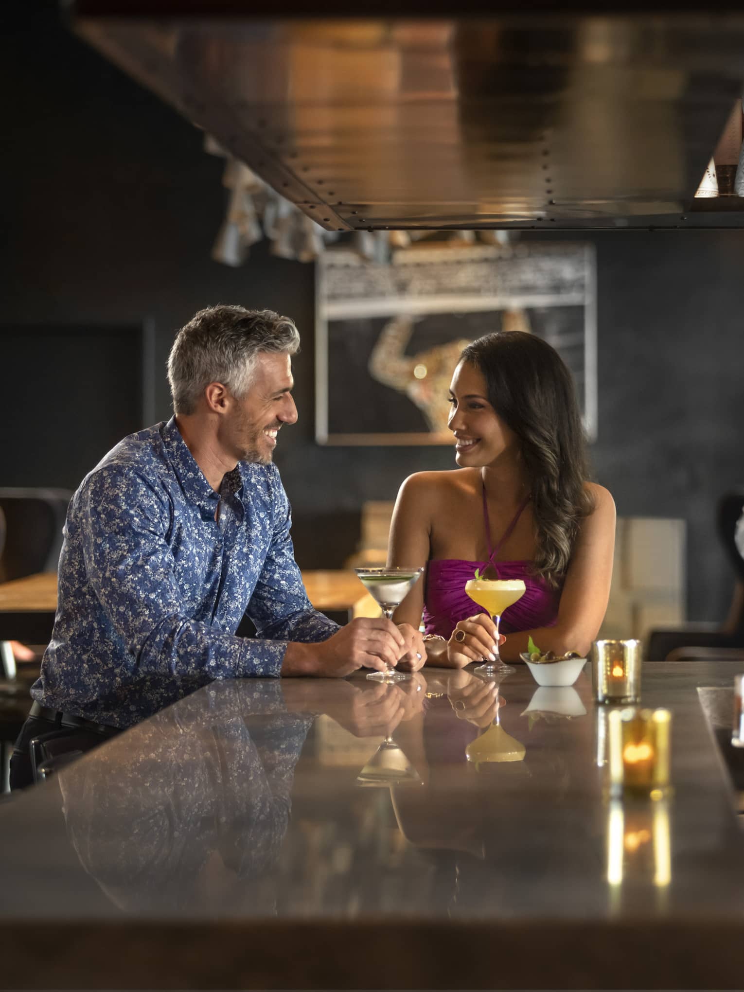 A couple sits at a bar counter as a bartender pours a drink