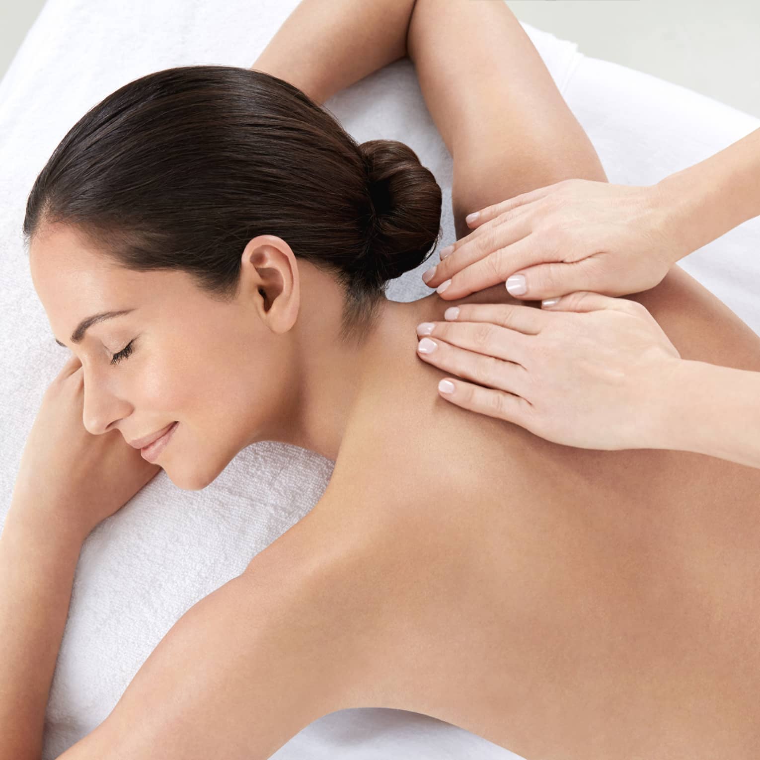 Woman smiles, lies on massage table as hands massage bare shoulders