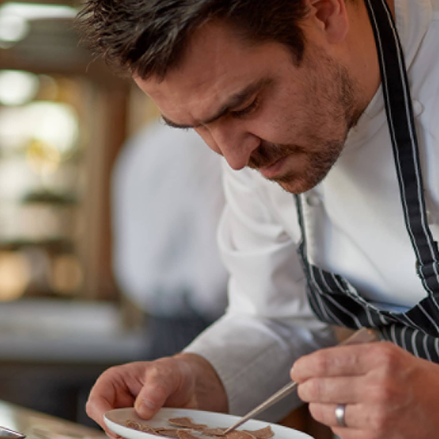 Four Seasons chef in striped apron carefully plating a dish in a kitchen