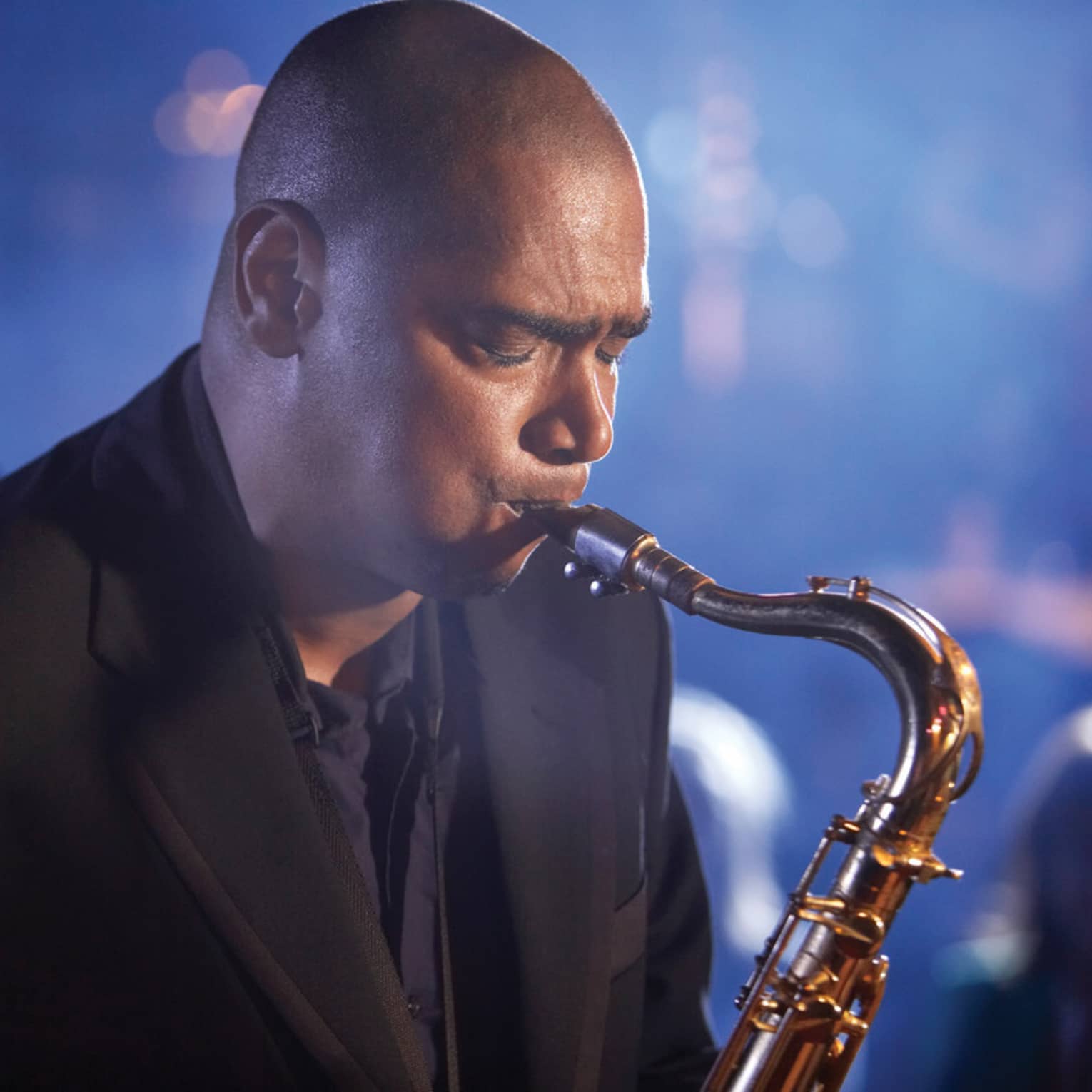 A close up of a man with his eyes closed, playing a saxaphone at a Jazz club in Ten Trinity