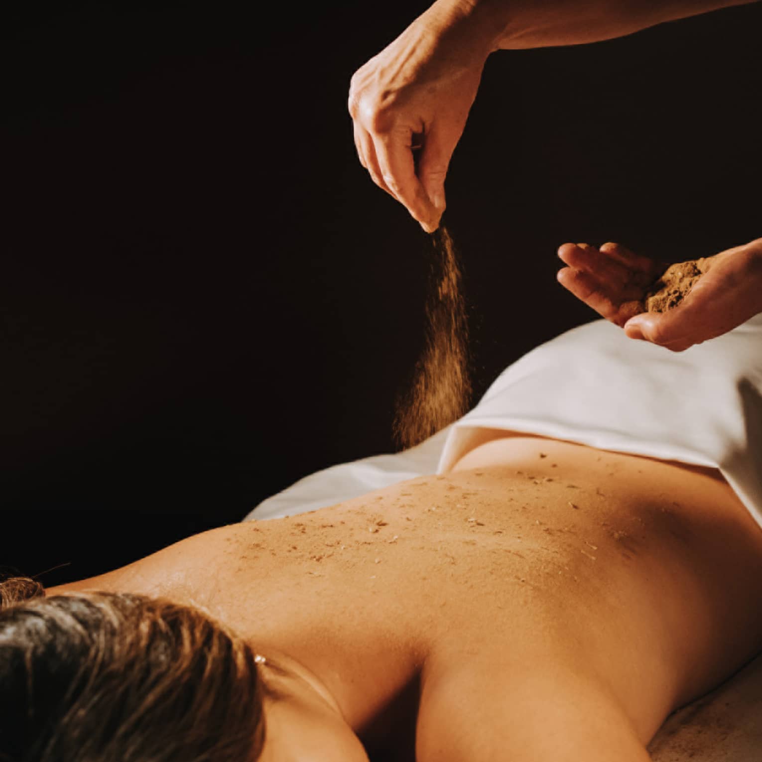 Spa staff sprinkled coffee powder over woman's bare back as she lays on massage table