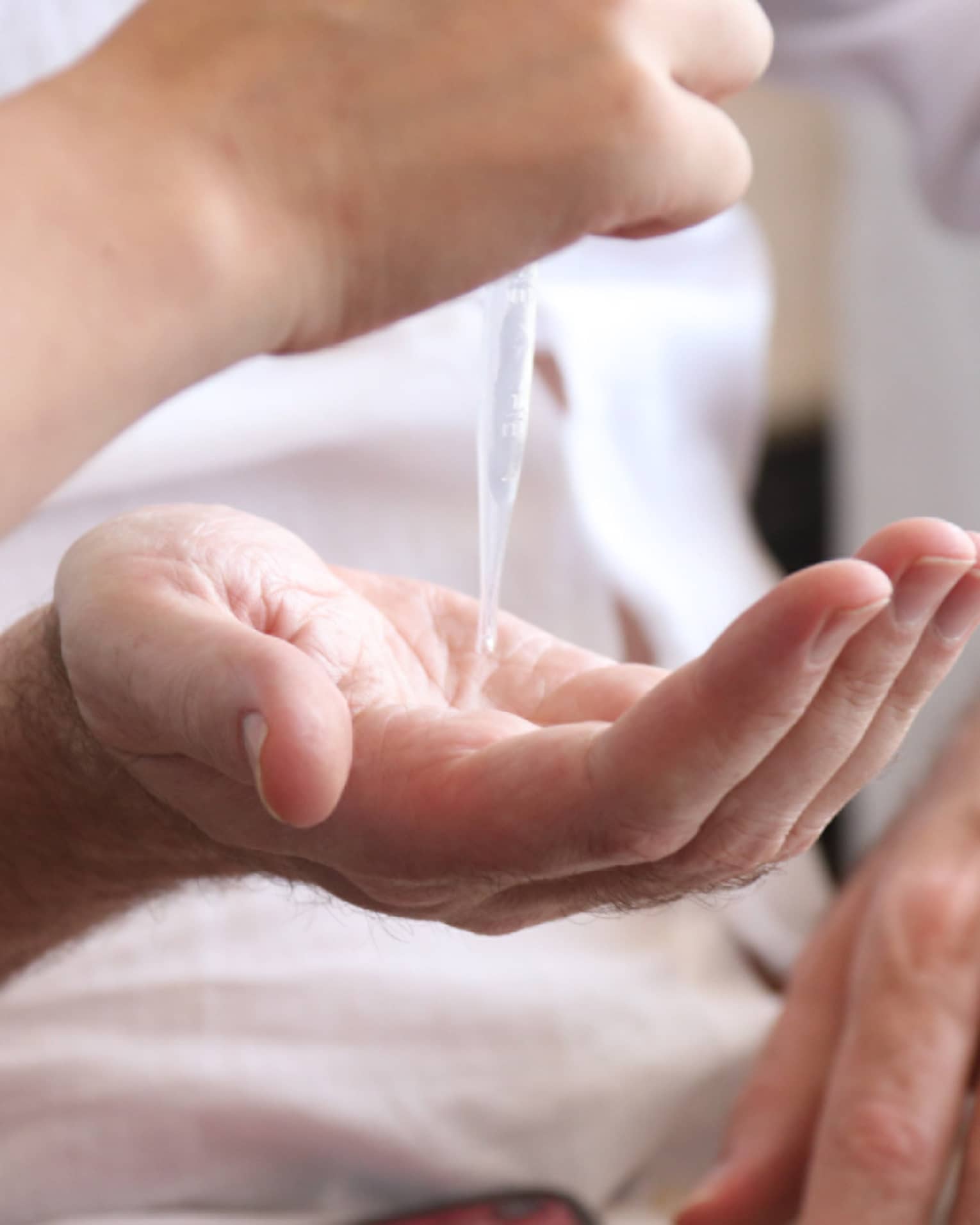A person holding out their hand while another person uses a syringe to drop an aromatherapy blend in their hand
