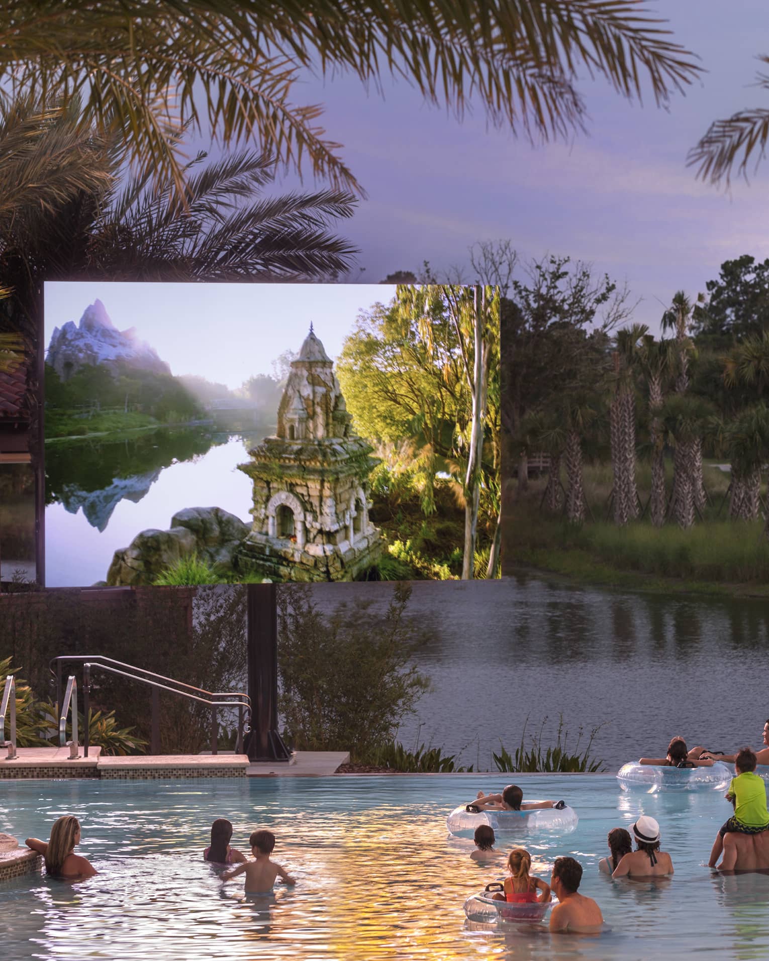 Under a dusk grey sky, adults and children watch a large outdoor screen while wading in a pool bordered by palm trees.
