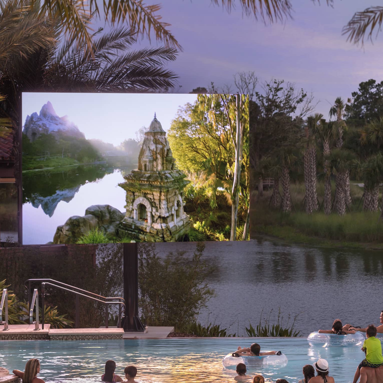 Under a dusk grey sky, adults and children watch a large outdoor screen while wading in a pool bordered by palm trees.