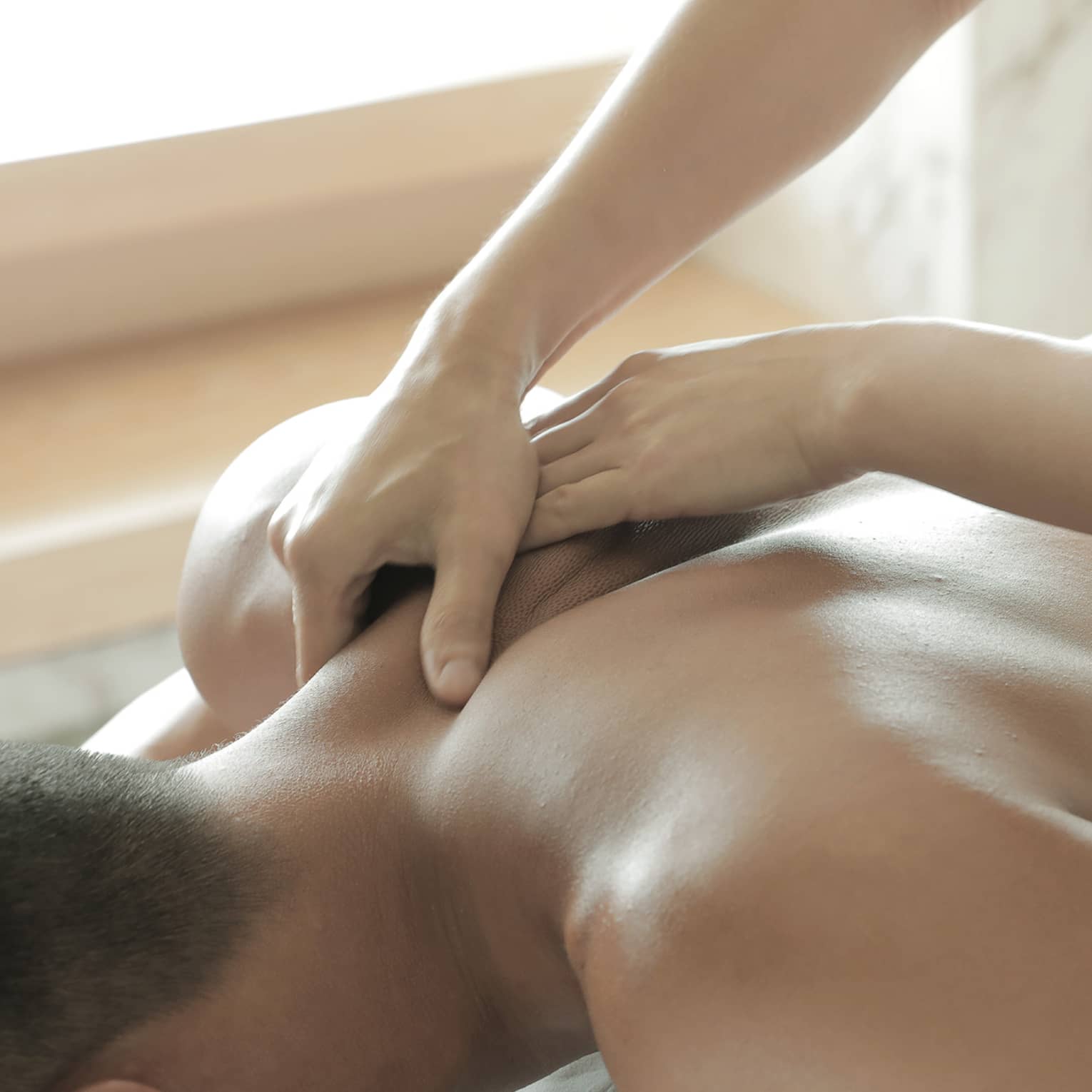 Spa masseuse massages man's bare back, shoulders