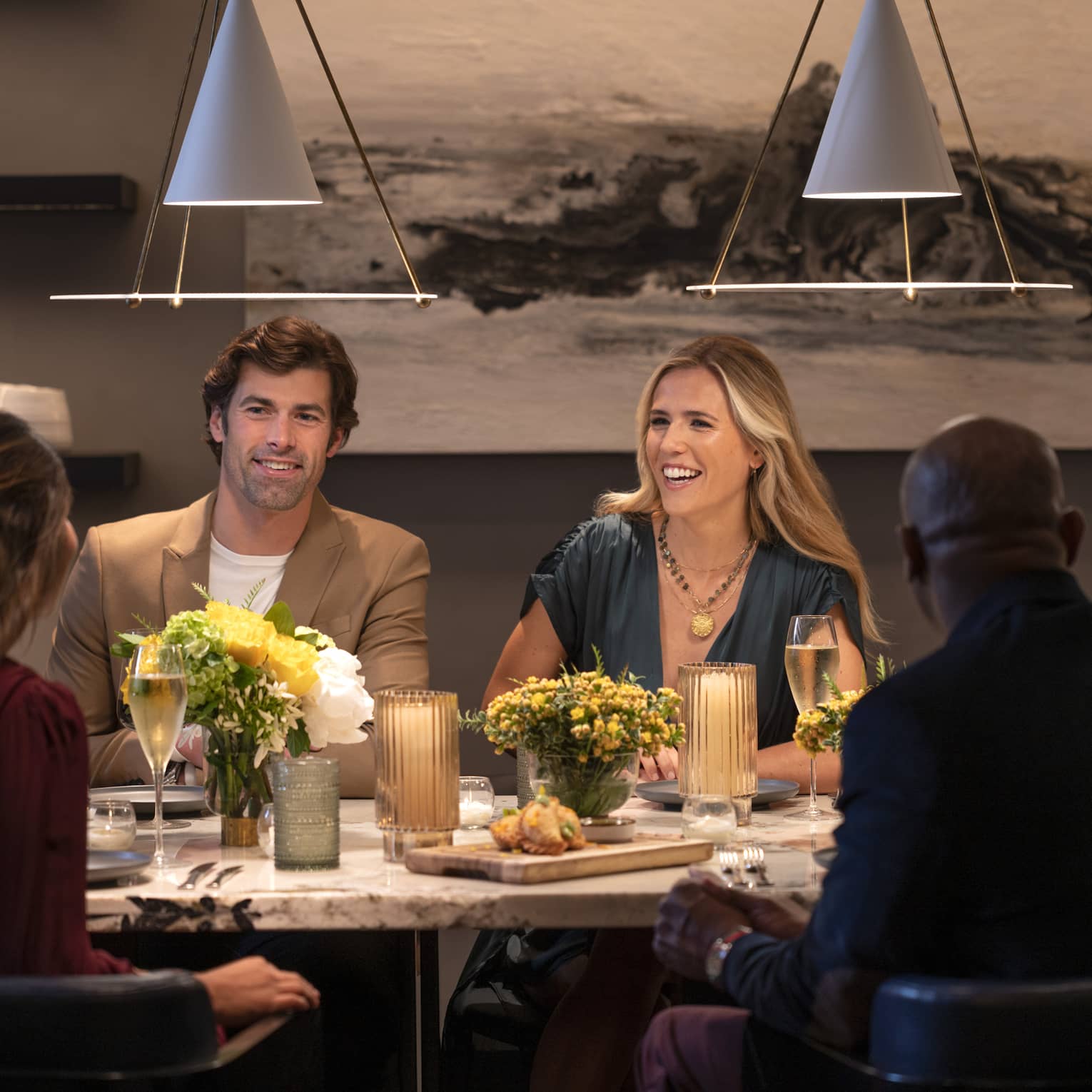 Guests sitting at a table and smiling at each other at a restaurant with overhead lighting