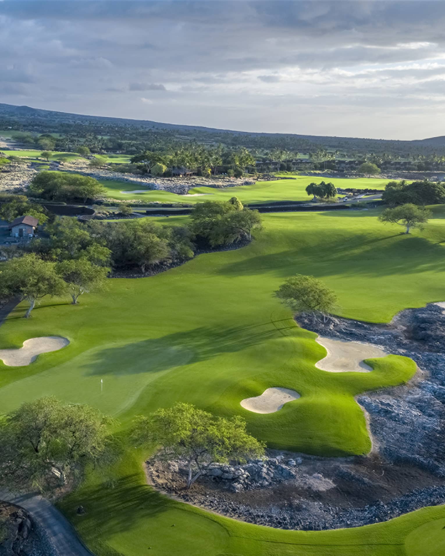 An overhead view of a lush green golf course under a cloudy sky.