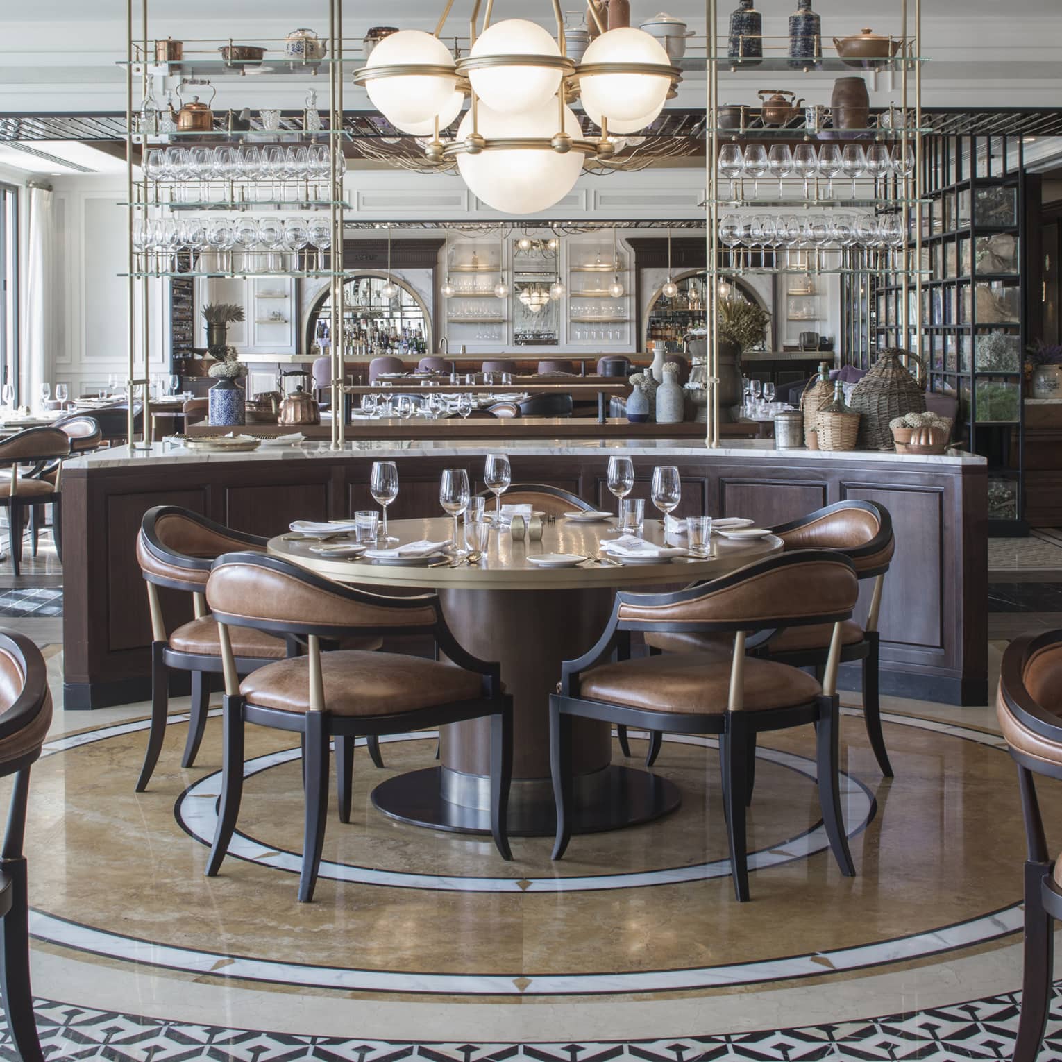An art-deco restaurant features tables with low-back brown-leather chairs and a counter with copper kettles and wicker jugs.