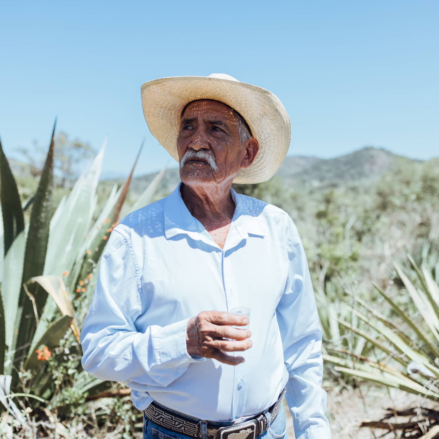 Person wearing a hat and a blue button down shirt standing outside.