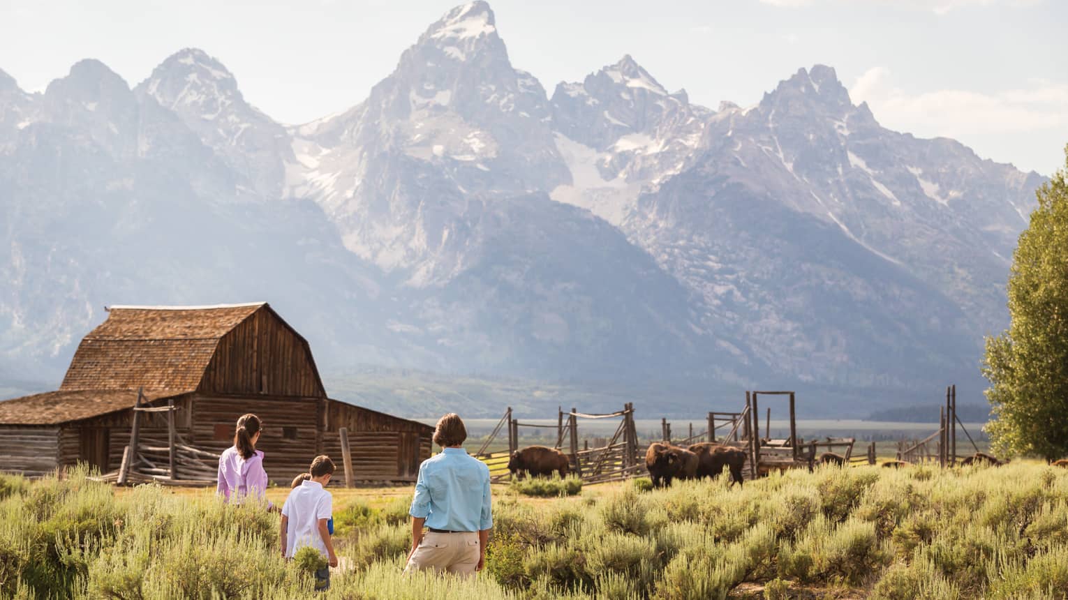 Family standing in a field with a cabin and mountains in the background.