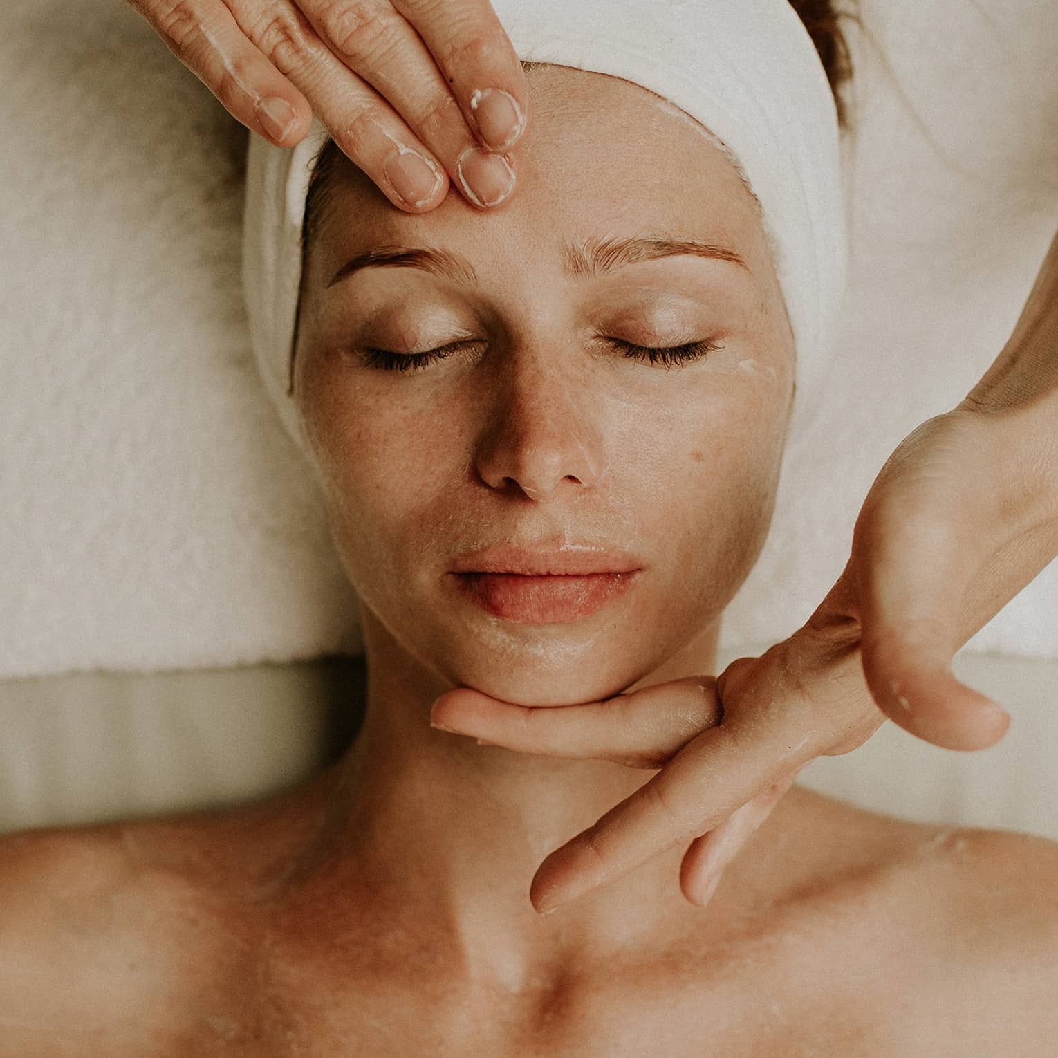 Person receiving a relaxing facial massage with eyes closed and head wrapped in a towel