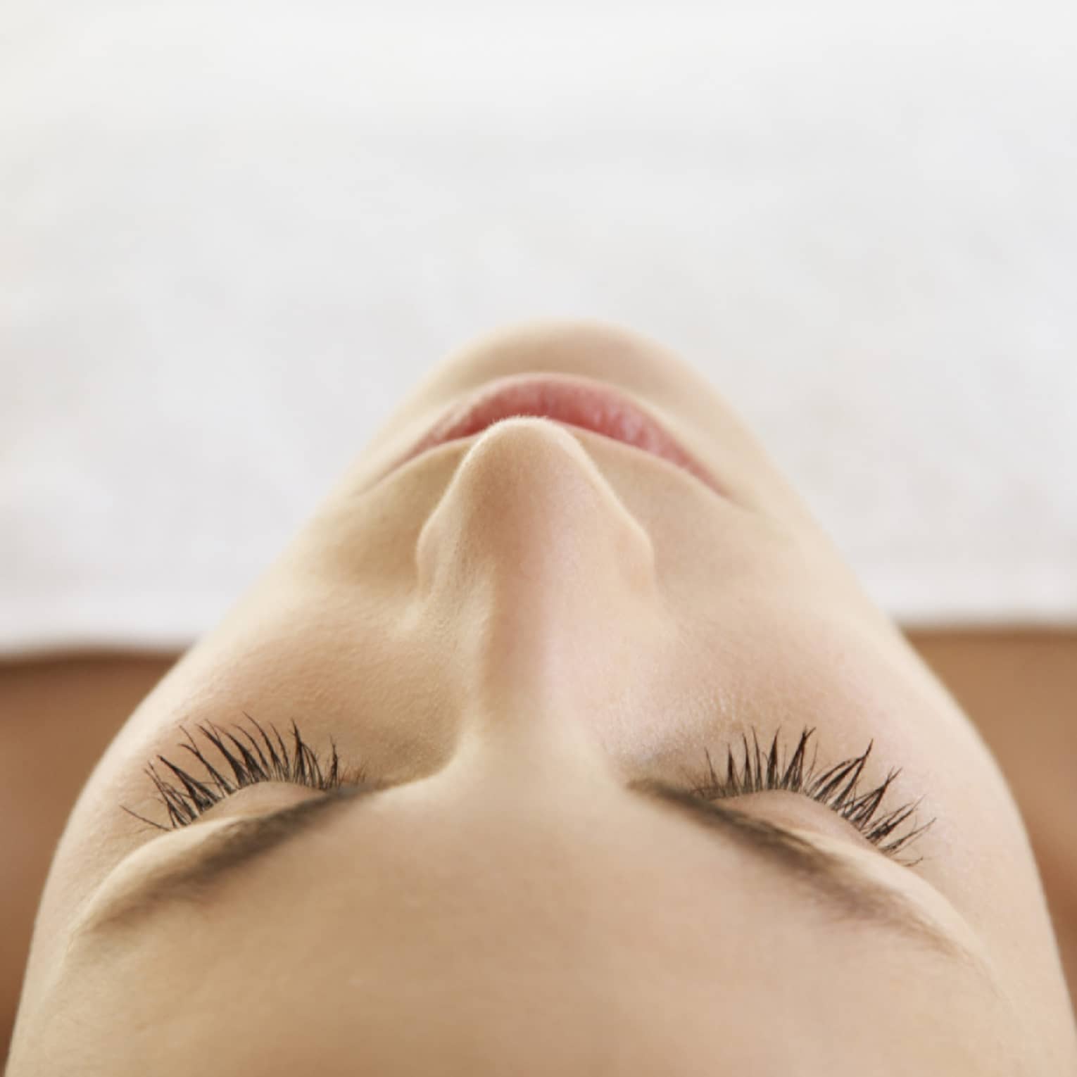 Woman lying down with eyes closed, bare shoulders, covered with white sheet